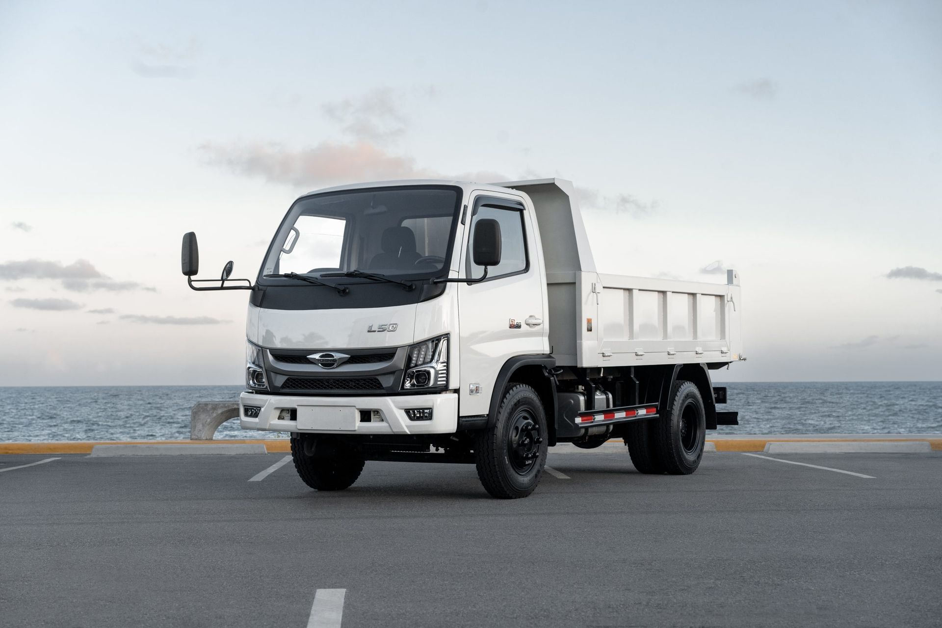 A white dump truck is parked on the side of the road near the ocean.