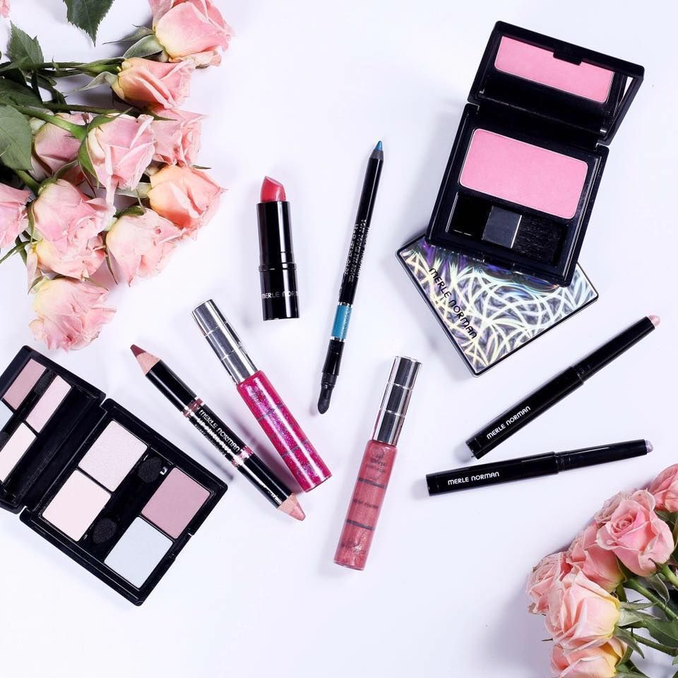 Makeup products and pink roses arranged on a white surface.