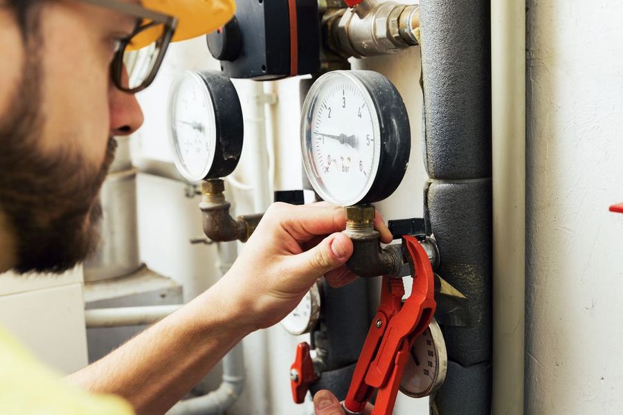 Tecnico che regola una valvola su tubazioni industriali con manometri e attrezzi rossi nelle vicinanze.