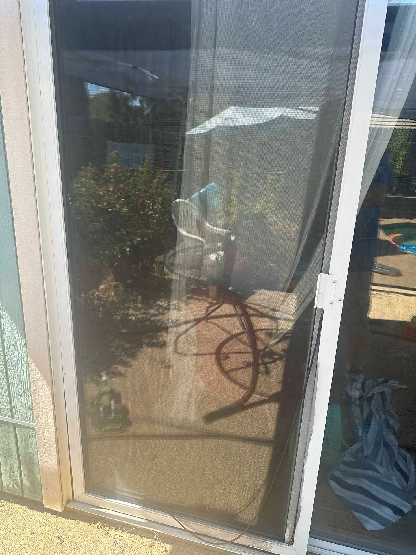 Reflection of a bicycle in a glass patio door beside a white outdoor chair.