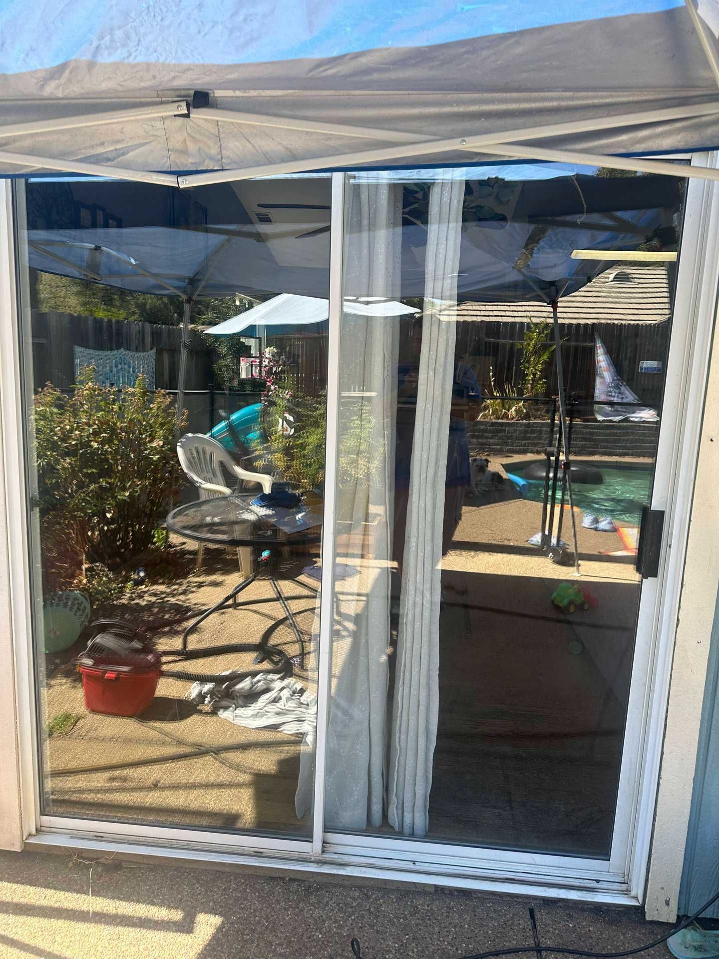 Patio seen through glass doors, with a person seated under a beige canopy and potted plants nearby