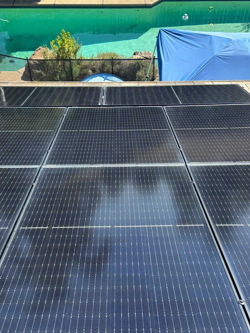 Solar panels on a rooftop with a green wall and a blue tarp in the background