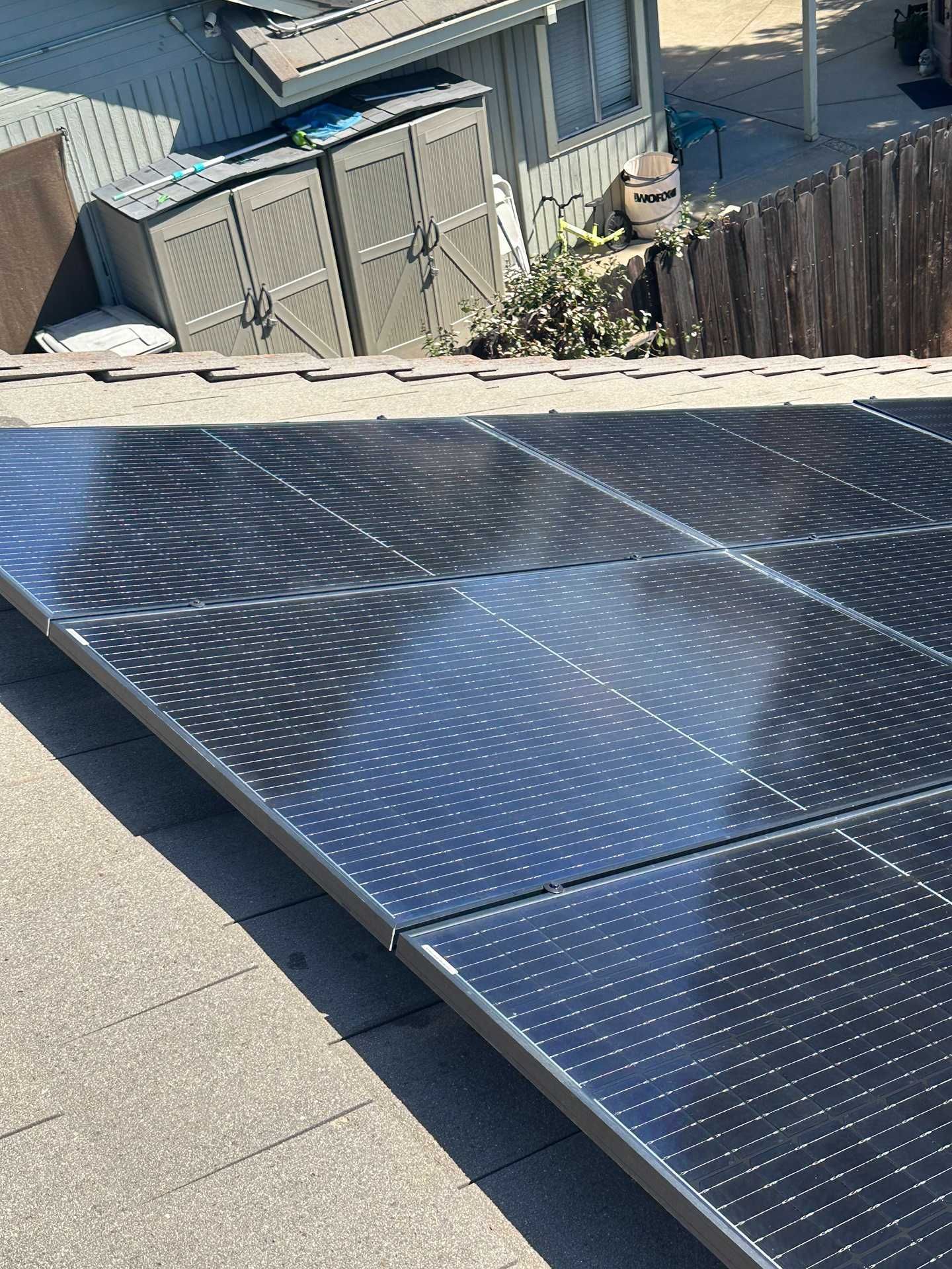 Solar panels on a rooftop with a corrugated shed and yard in the background.