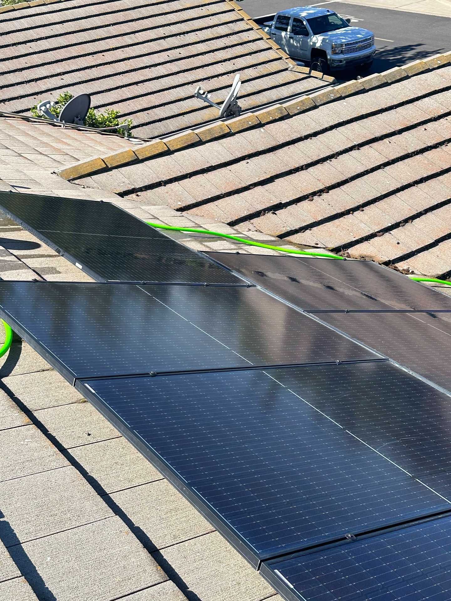 Roof with dark solar panels installed on tan shingles, with roof workers and tools visible nearby