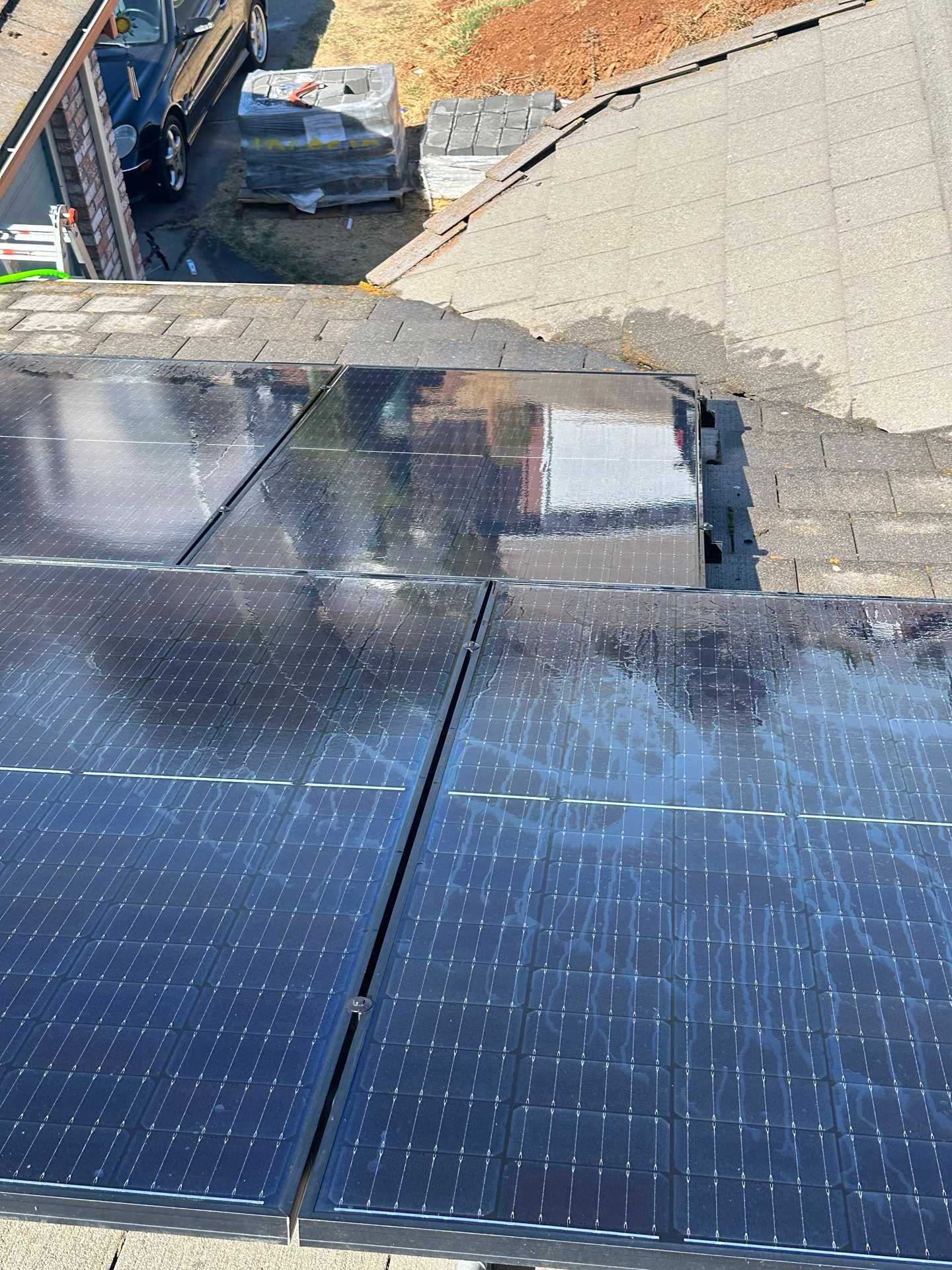 Solar panels on a rooftop with a small building and parked car below, viewed from above.