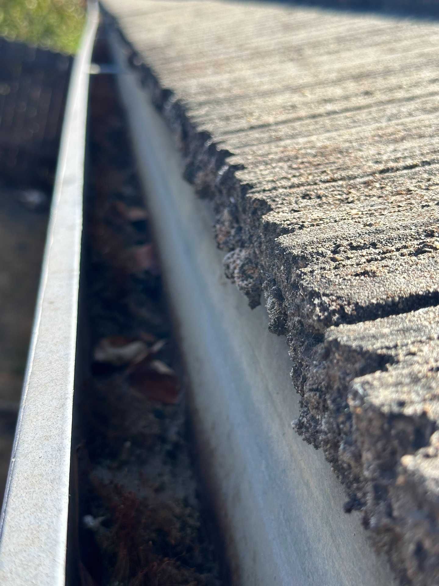 Close-up of a metal gutter beside a sunlit rough concrete edge with debris below