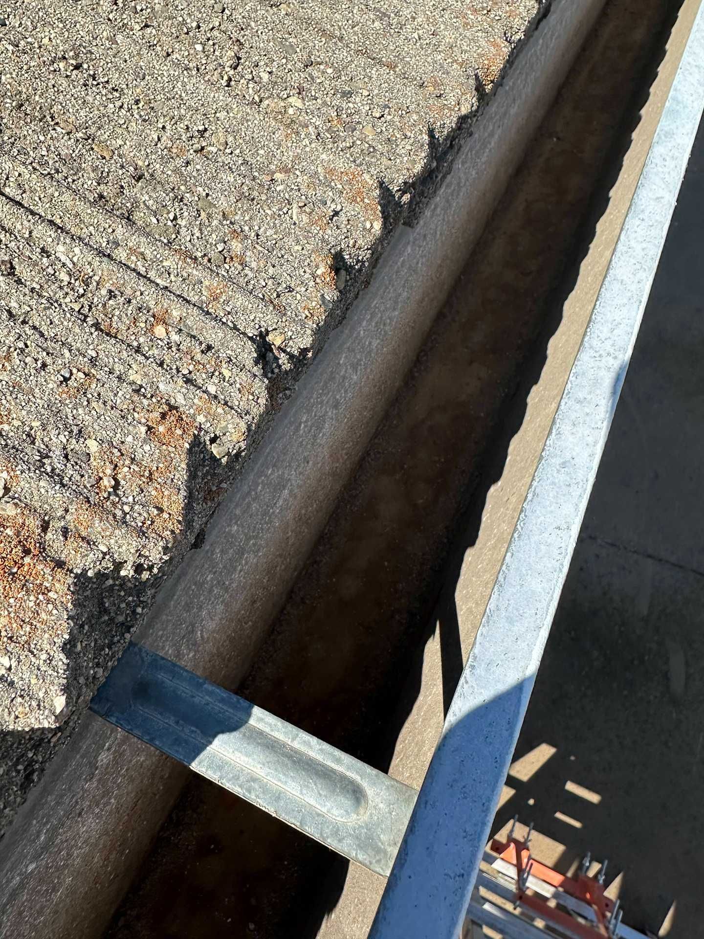 Close-up of a roof edge with a metal gutter and a ladder leaning up beside it.