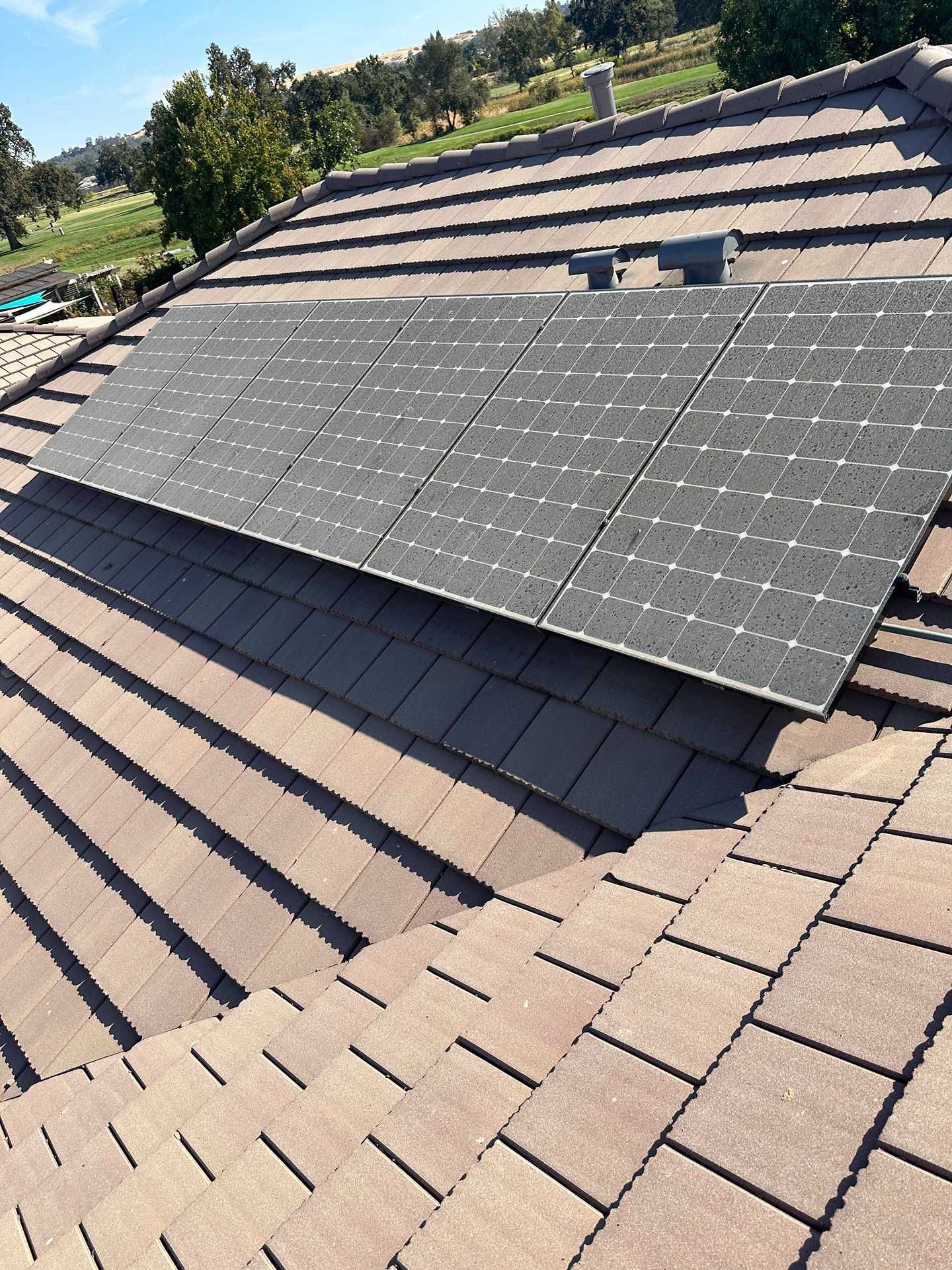 Solar panels mounted on a brown shingled rooftop under a clear sky.