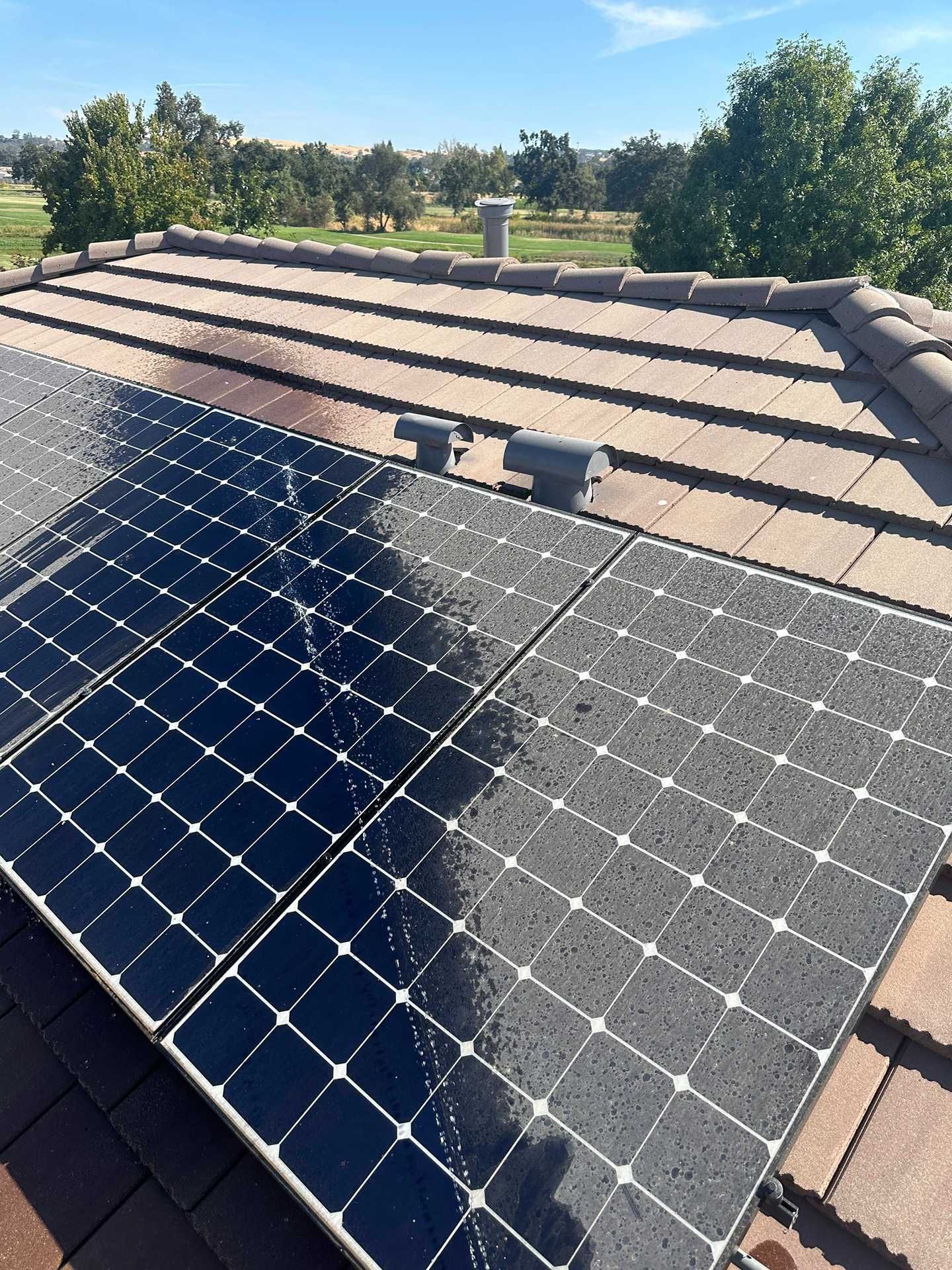 Solar panels installed on a tiled roof under a clear blue sky, with trees in the background.