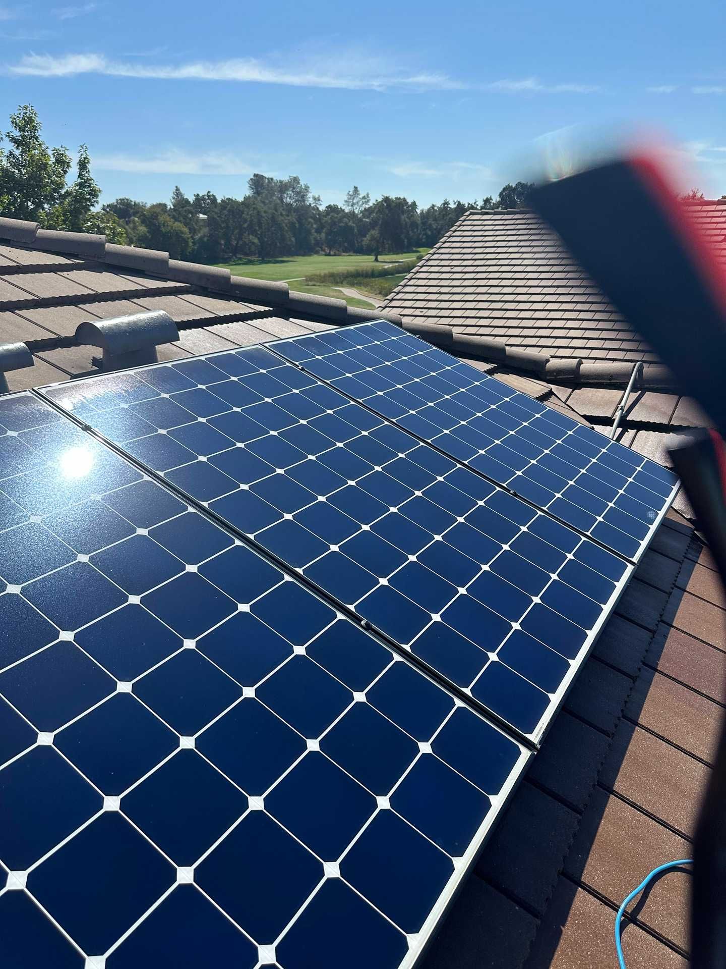 Solar panels mounted on a tiled roof under a clear blue sky, with trees in the background.