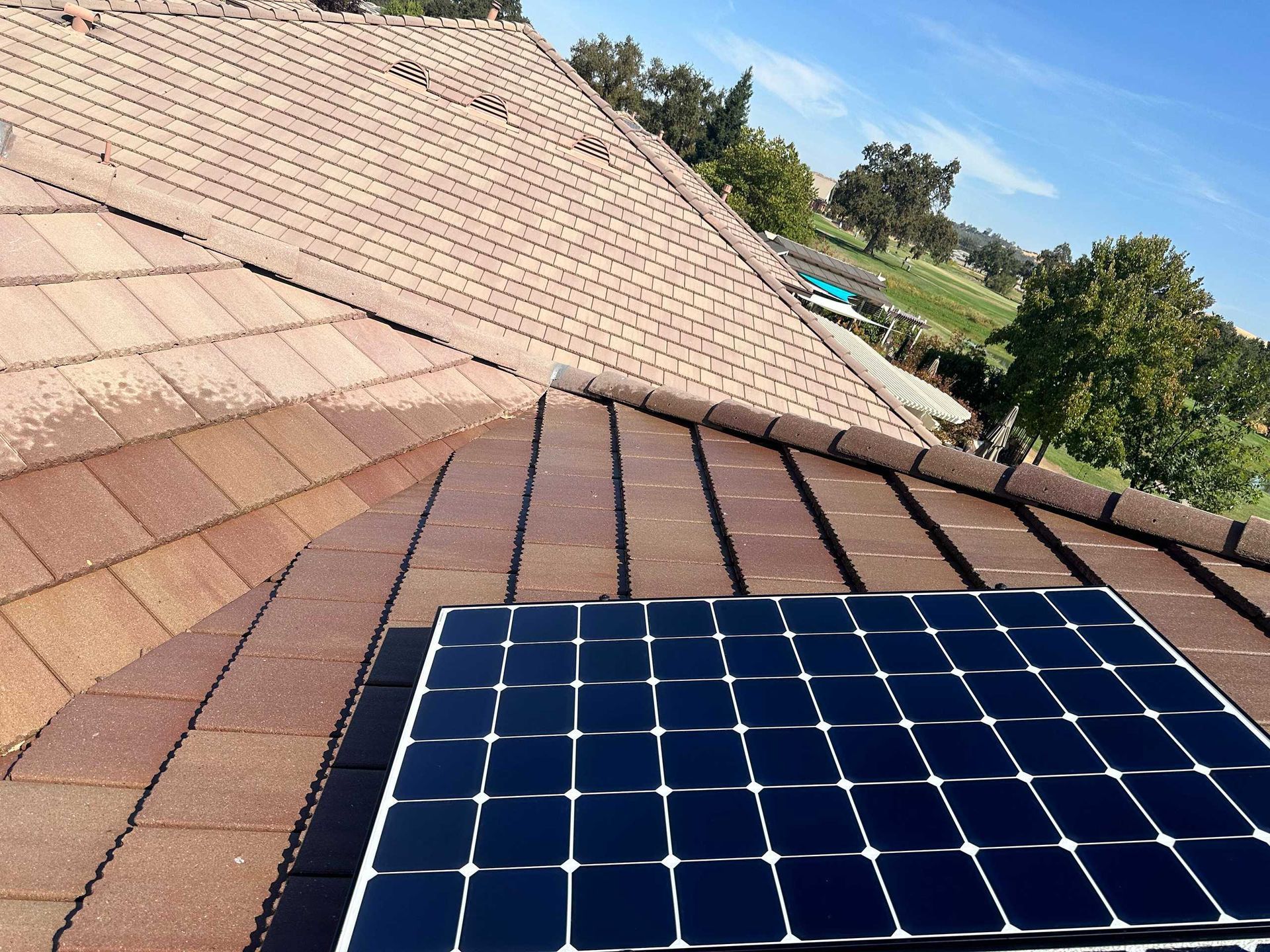 Solar panels mounted on a sloped shingle roof under a clear blue sky