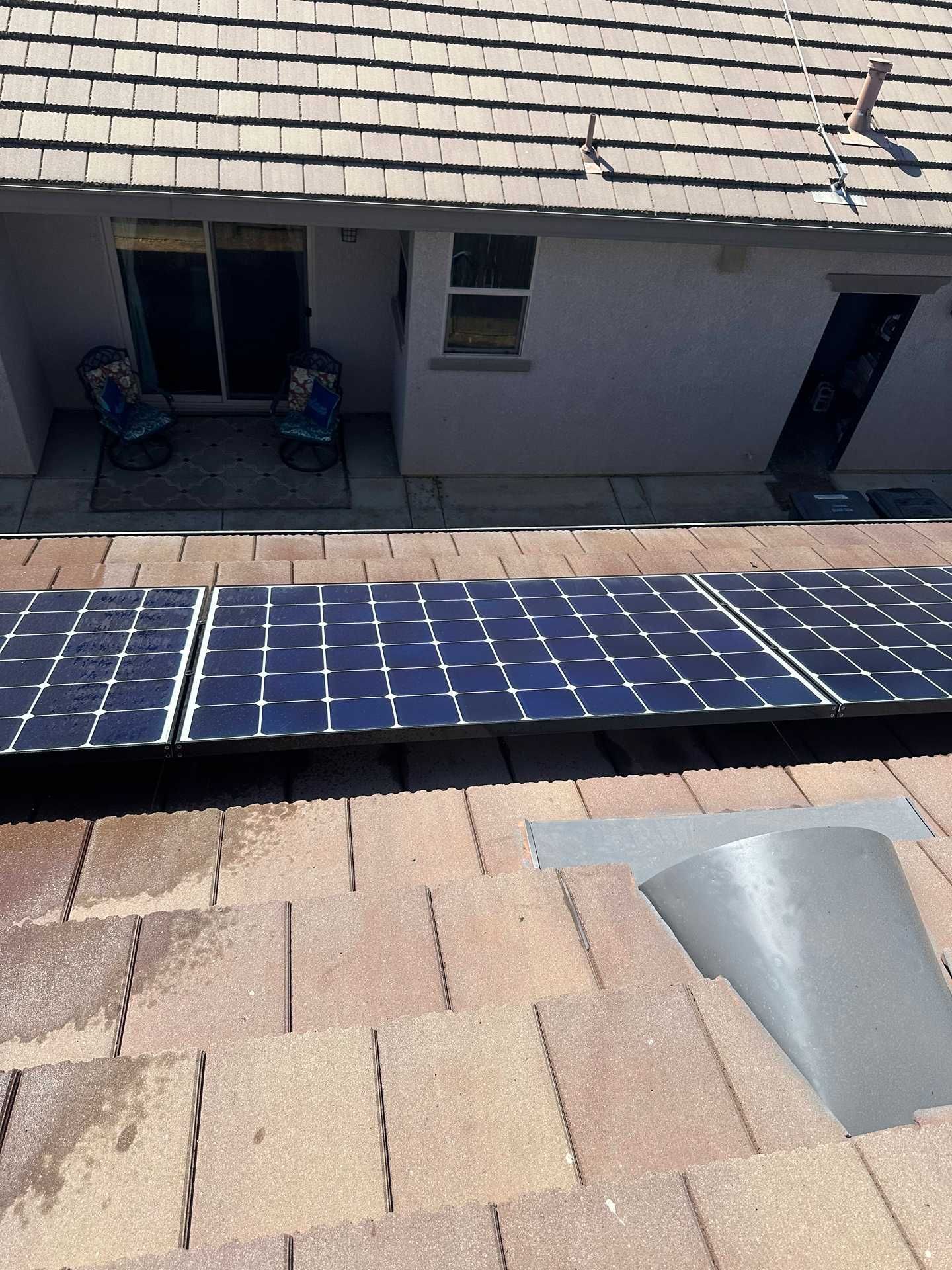 Rooftop solar panels on a shingled house, with a roof vent and windows in view.