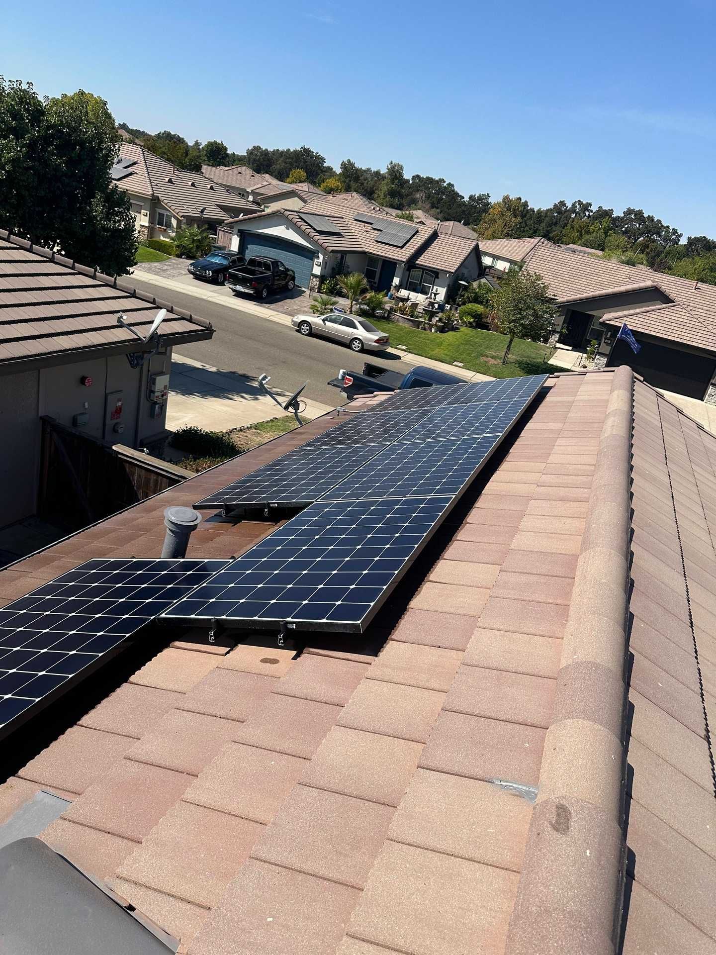 Solar panels mounted on a tan shingle roof in a suburban neighborhood under clear sunlight.