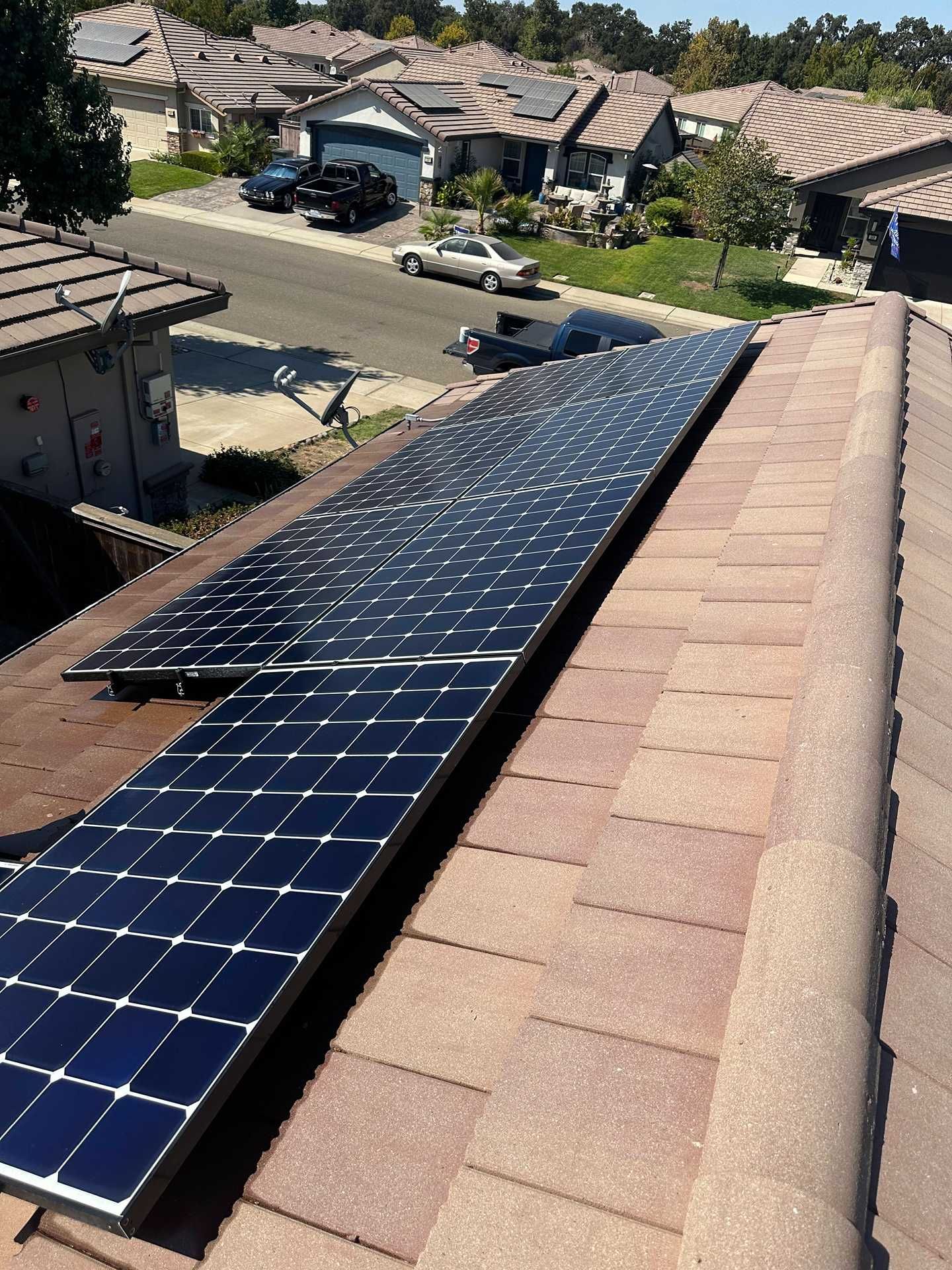 Rooftop solar panels on a suburban house with neighboring homes and parked cars below.