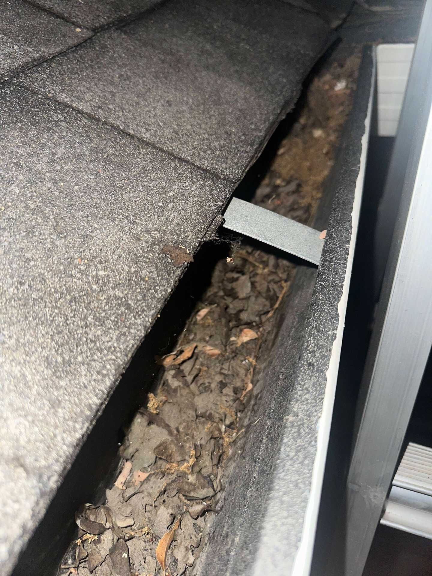 Damaged roof shingle with a gap exposing debris and a nearby metal vent pipe