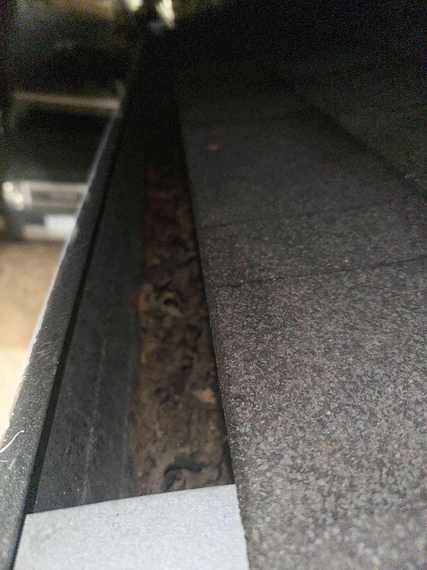 Close-up of a gutter filled with leaves beside a gray shingled roof at night
