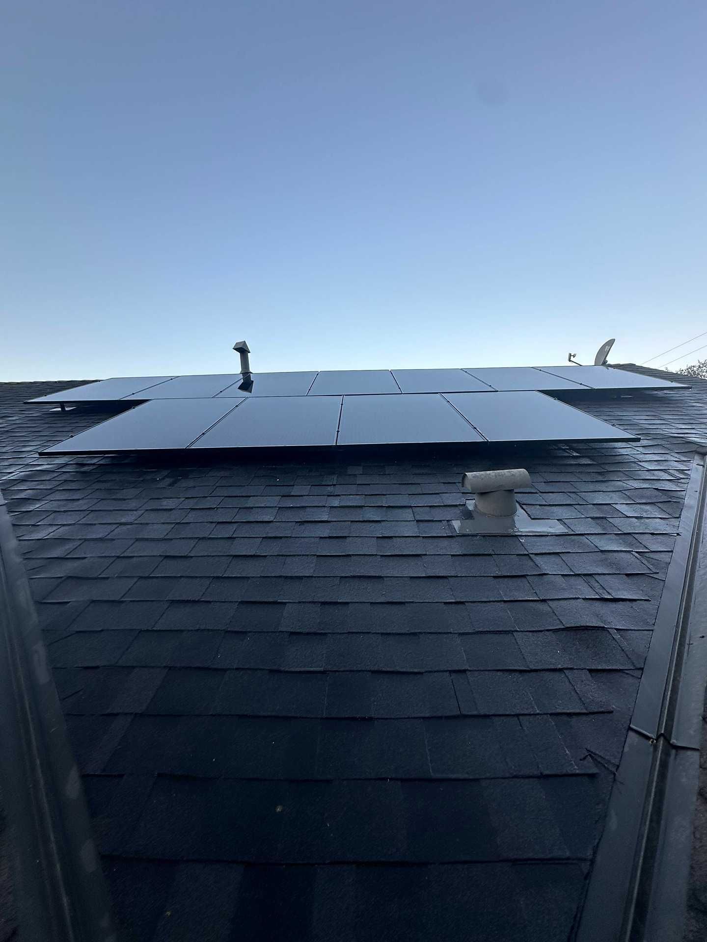 Solar panels mounted on a dark shingled roof under a clear blue sky