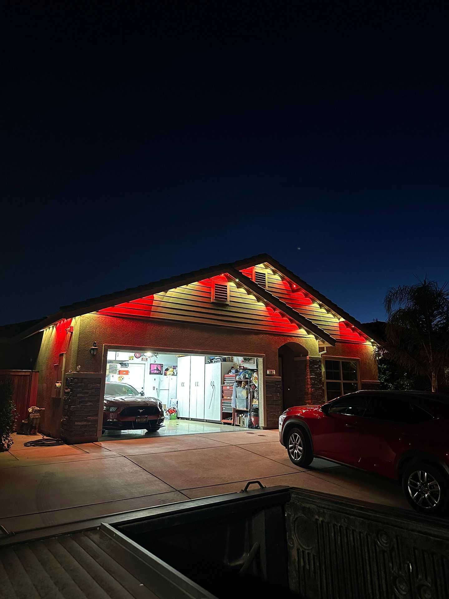 Well-lit garage at night with cars parked inside and in the driveway, red accent lights on the roof.