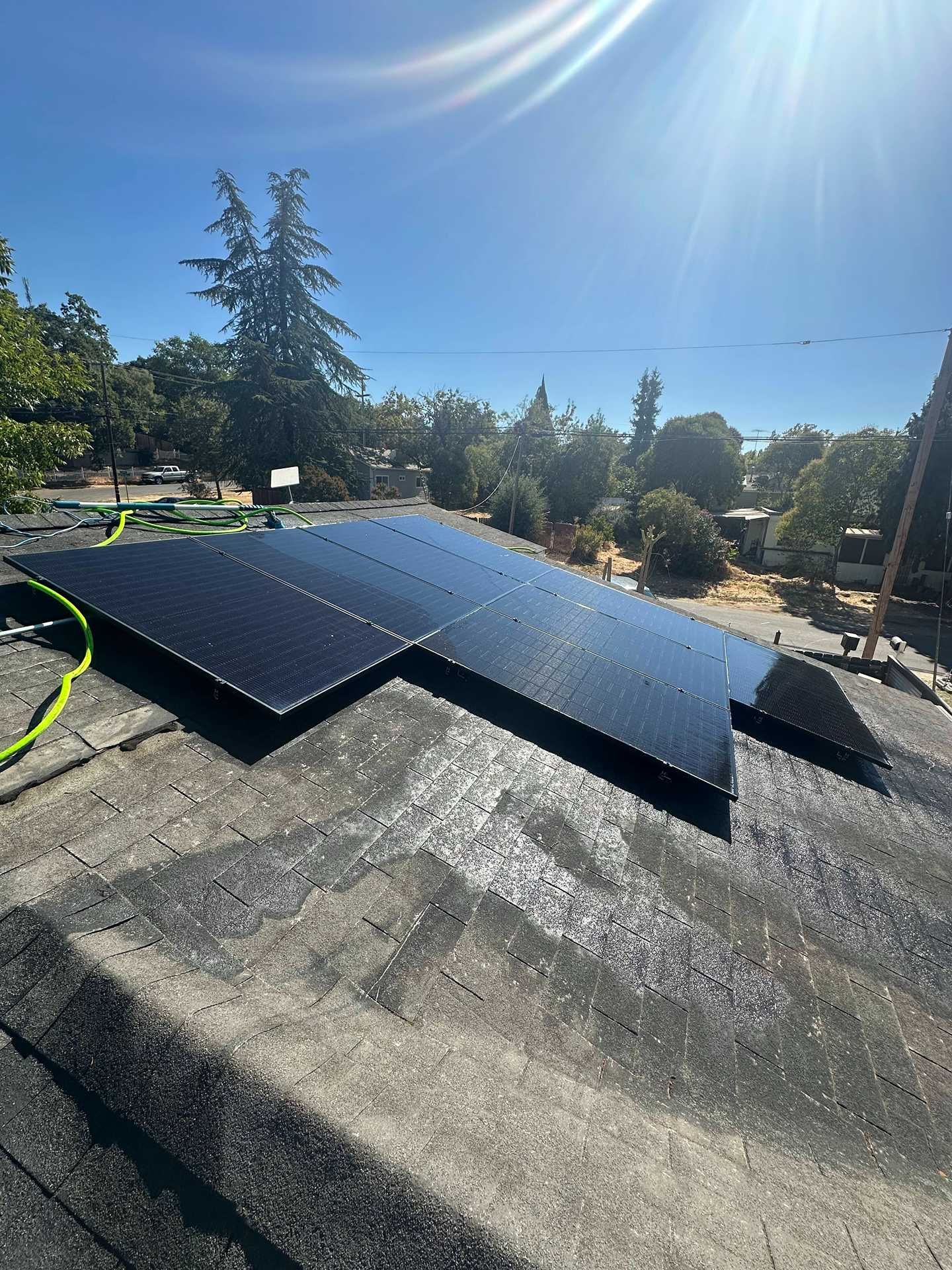 Solar panels installed on a shingled roof under a clear blue sky with bright sunlight.