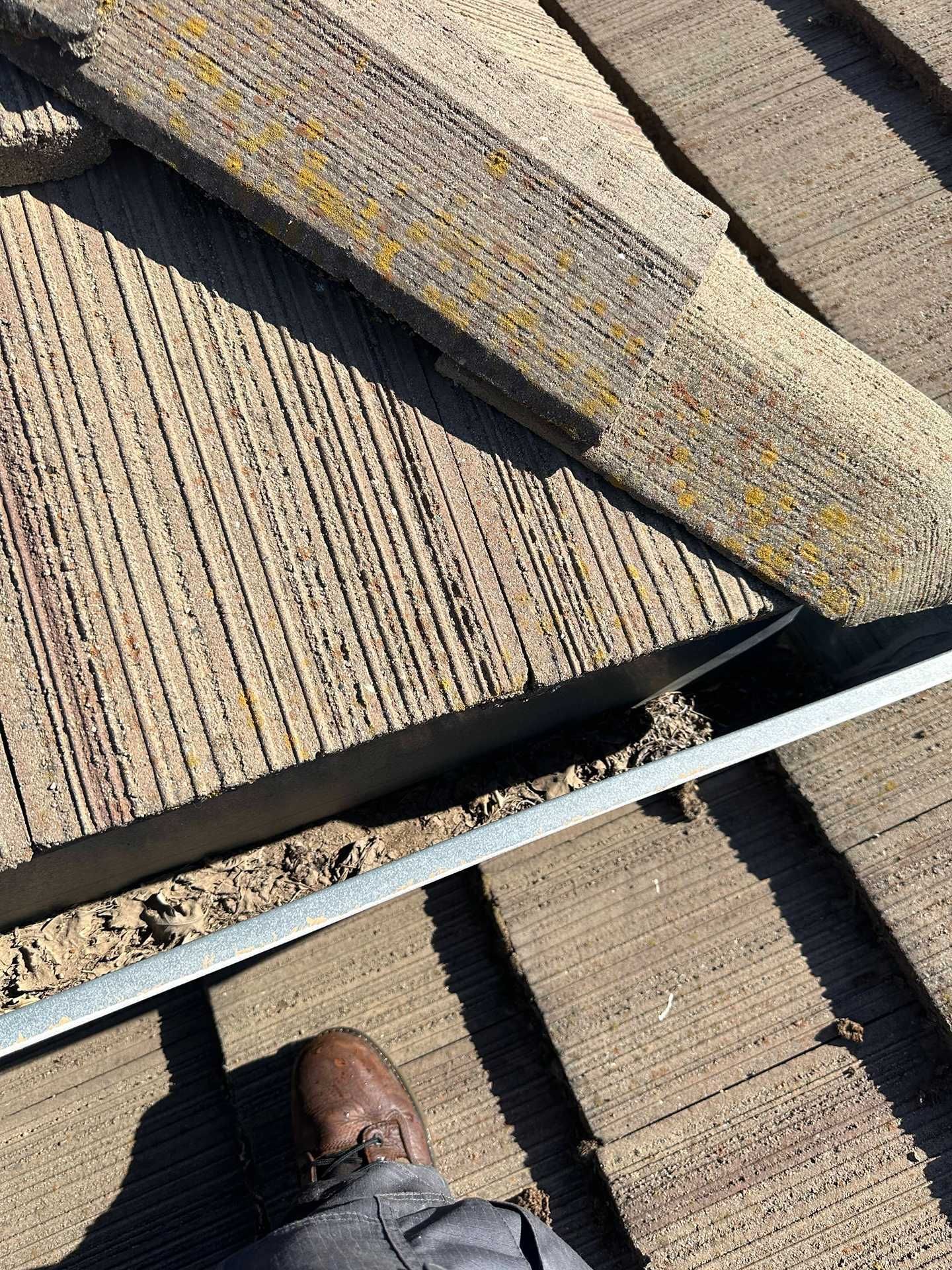 Person standing on tan rooftop shingles, looking over a roof edge with a white trim strip.