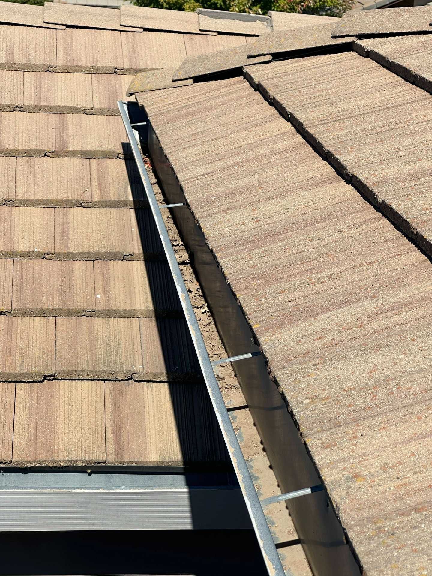 Damaged roof with a gap between shingle sections and exposed flashing along the seam