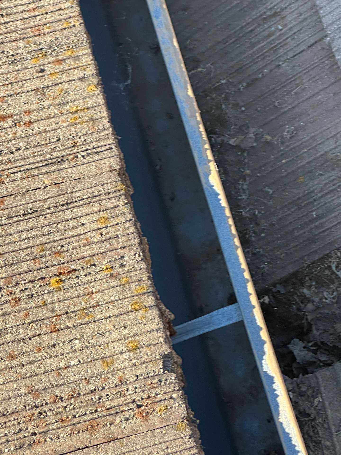 Close-up of a roof seam with blue flashing between light and dark shingles