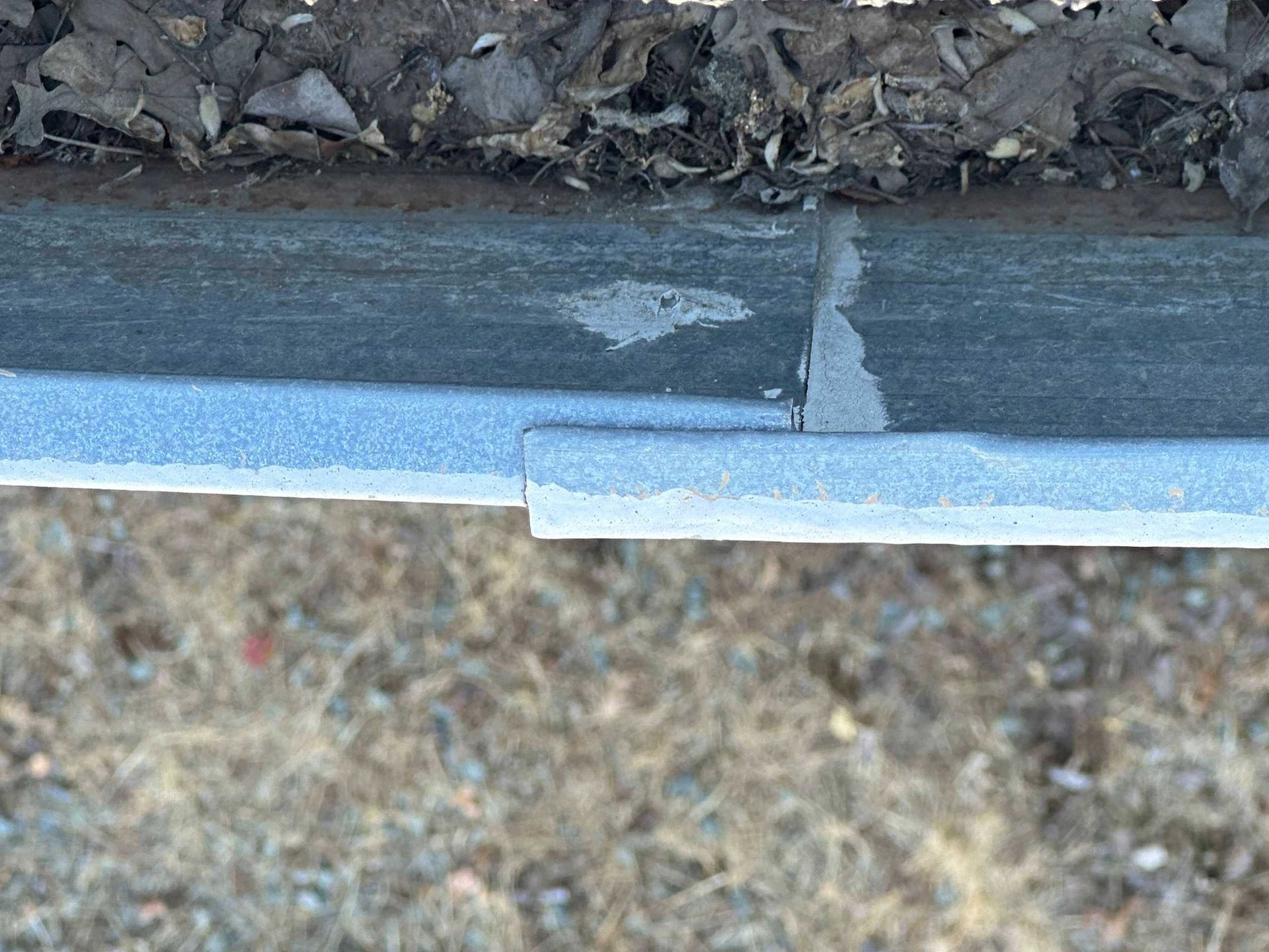 Close-up of a damaged asphalt seam beside a light blue metal edge trim.