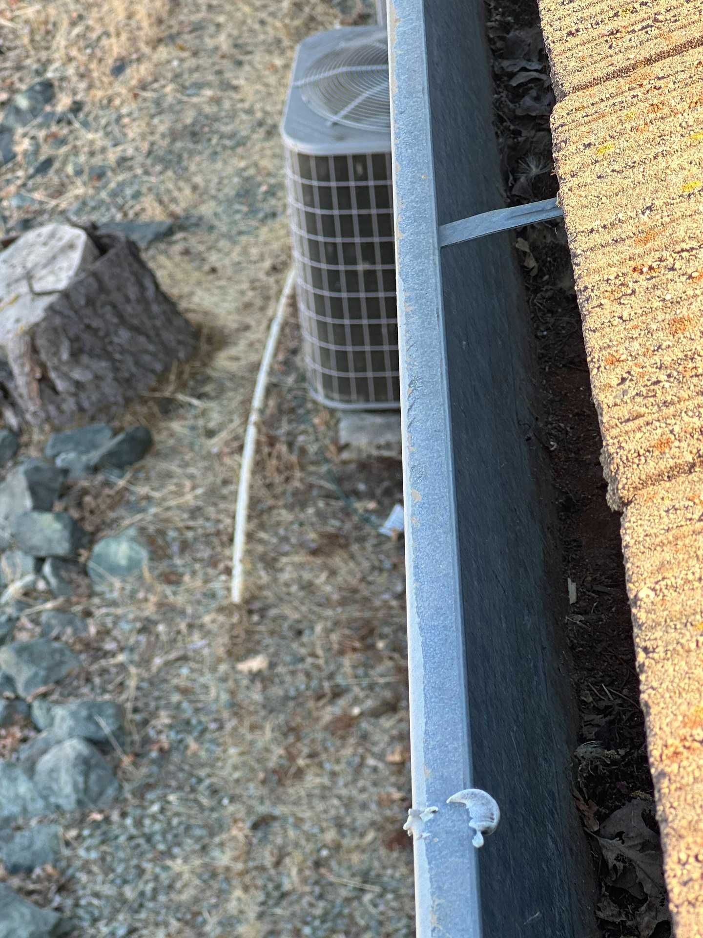 Outdoor AC unit beside a wall and gravel, with a white cable running along the ground.