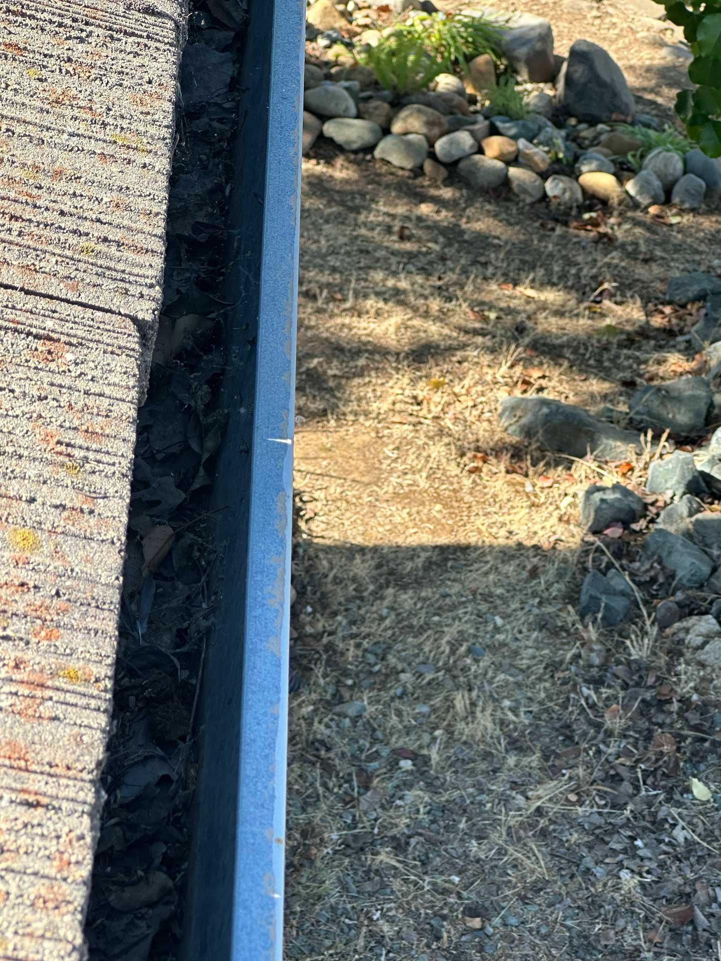 Roof edge gutter beside a gravel driveway and dry landscaping with rocks and sparse grass
