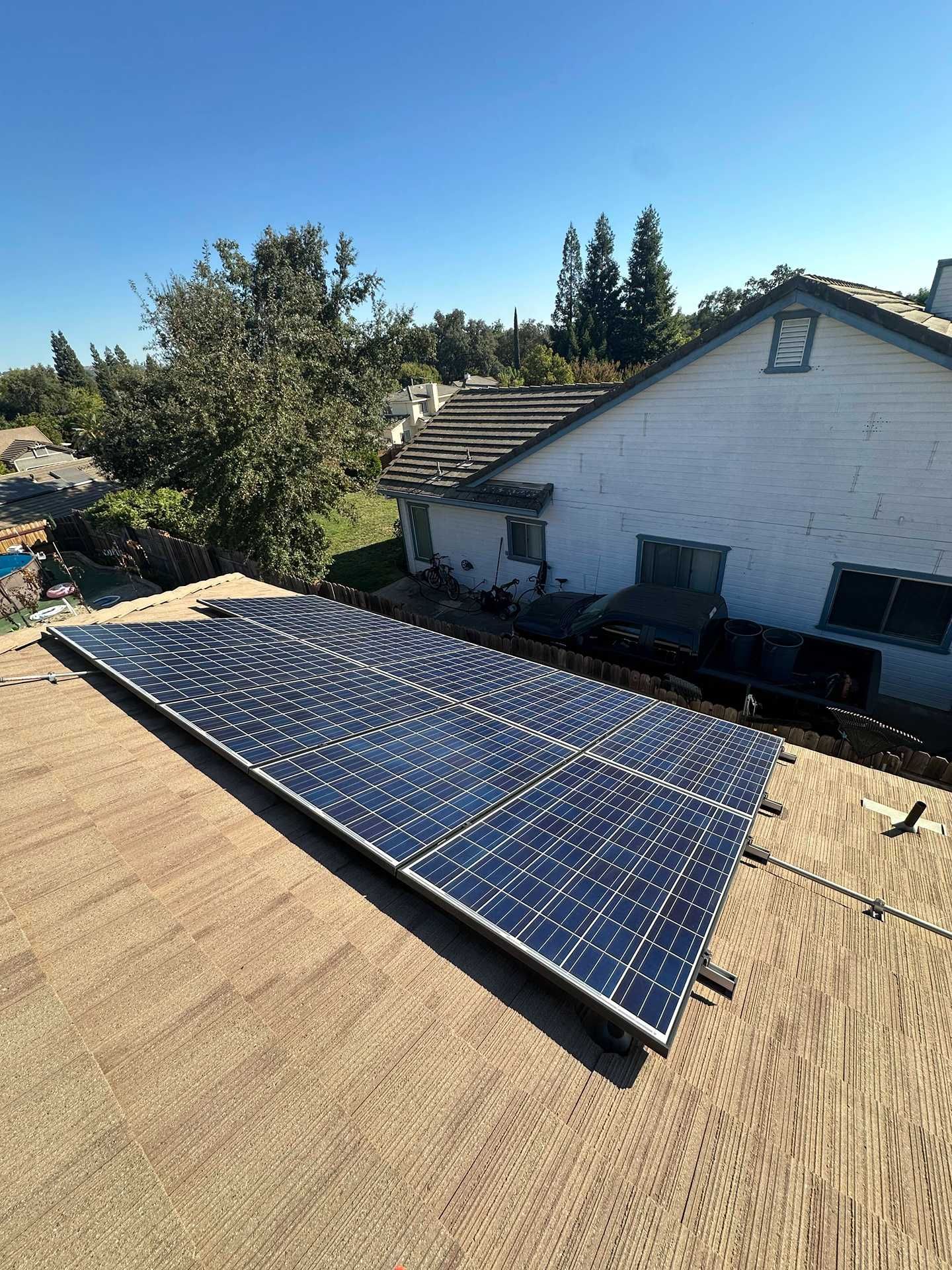 Solar panels mounted on a rooftop beside a white house under a clear blue sky