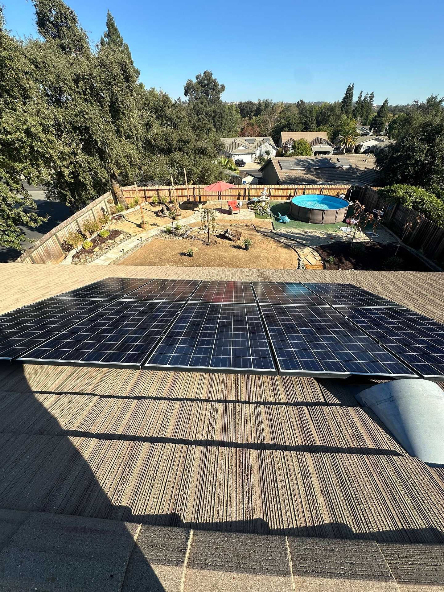 Solar panels on a rooftop overlooking a backyard with a pool and trees in the distance.
