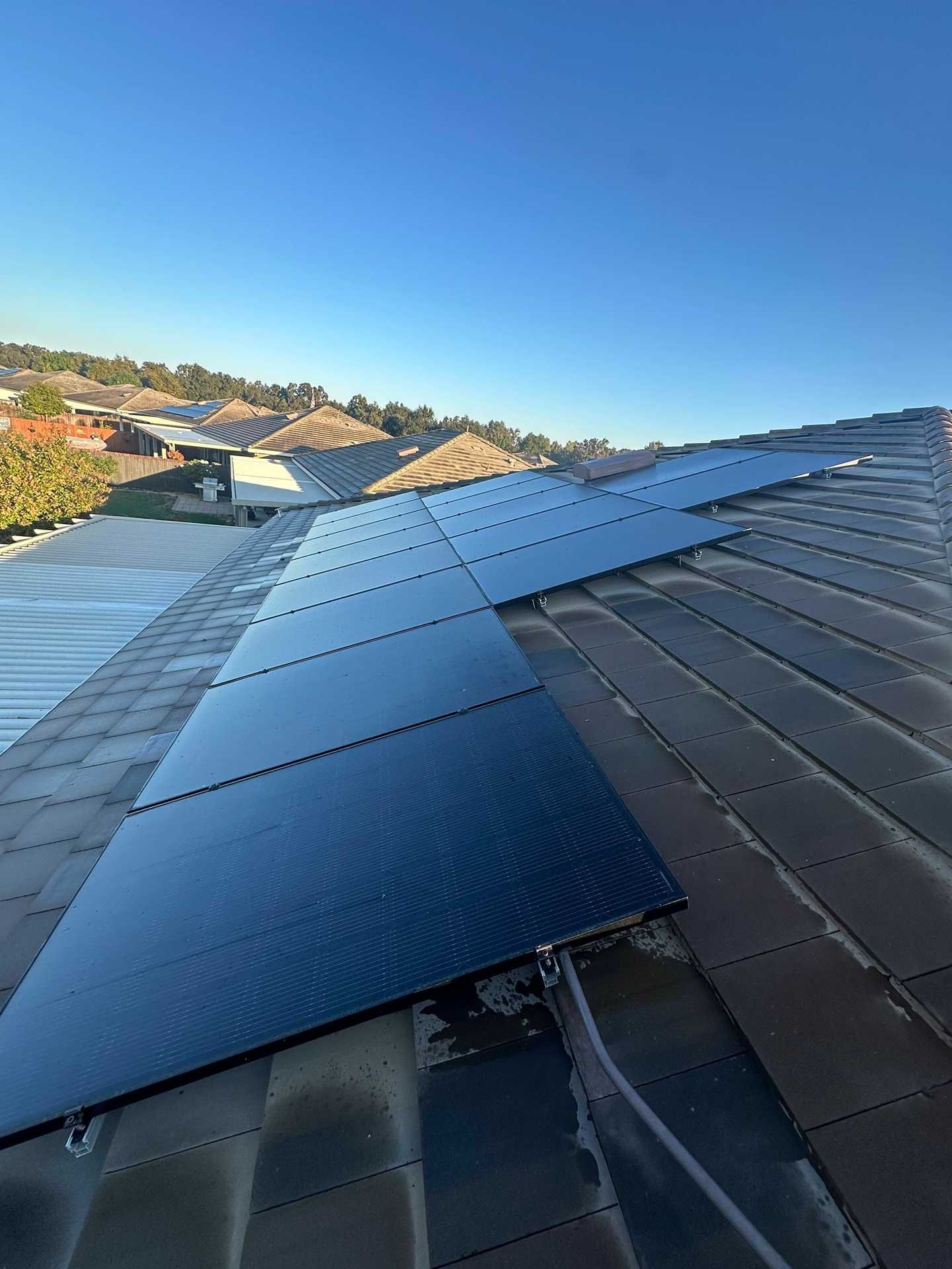 Solar panels installed in a row on a sloped rooftop under a clear blue sky.