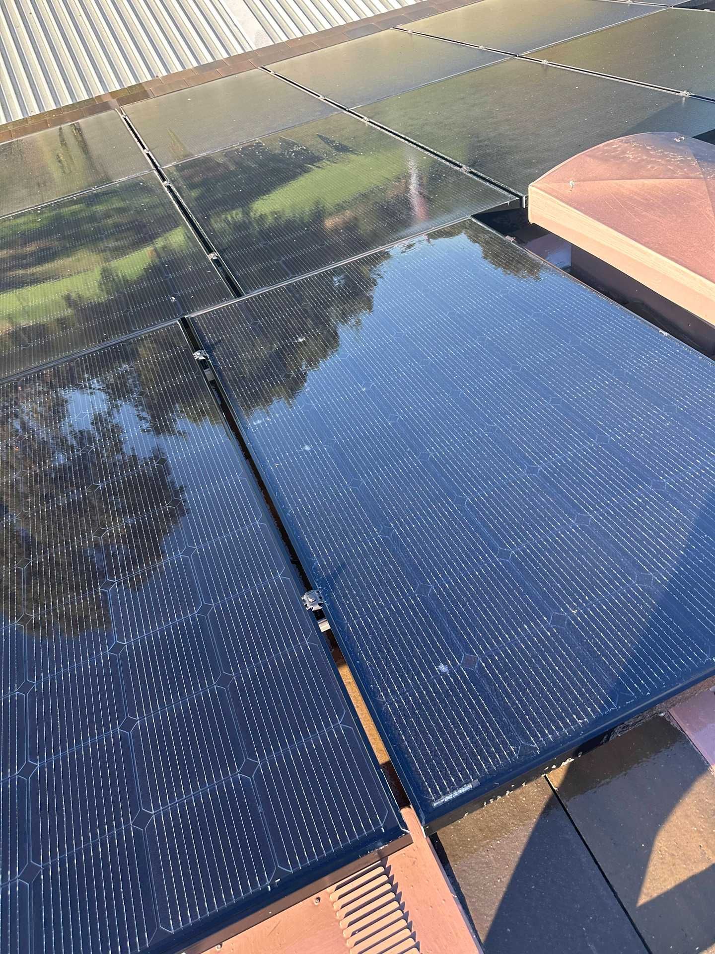 Glossy dark solar panels on a roof, reflecting the sky and nearby landscape