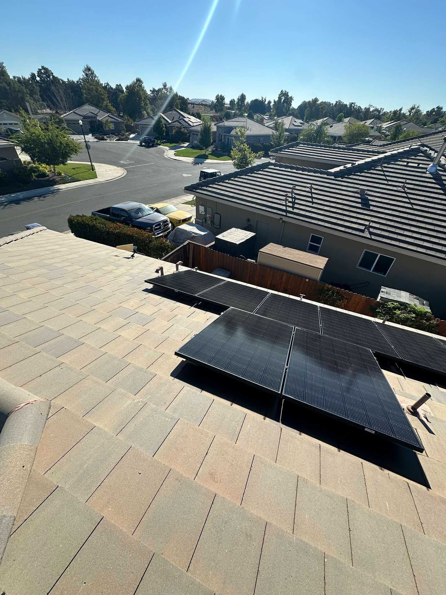 Solar panels on a shingled roof overlooking a sunny suburban neighborhood.