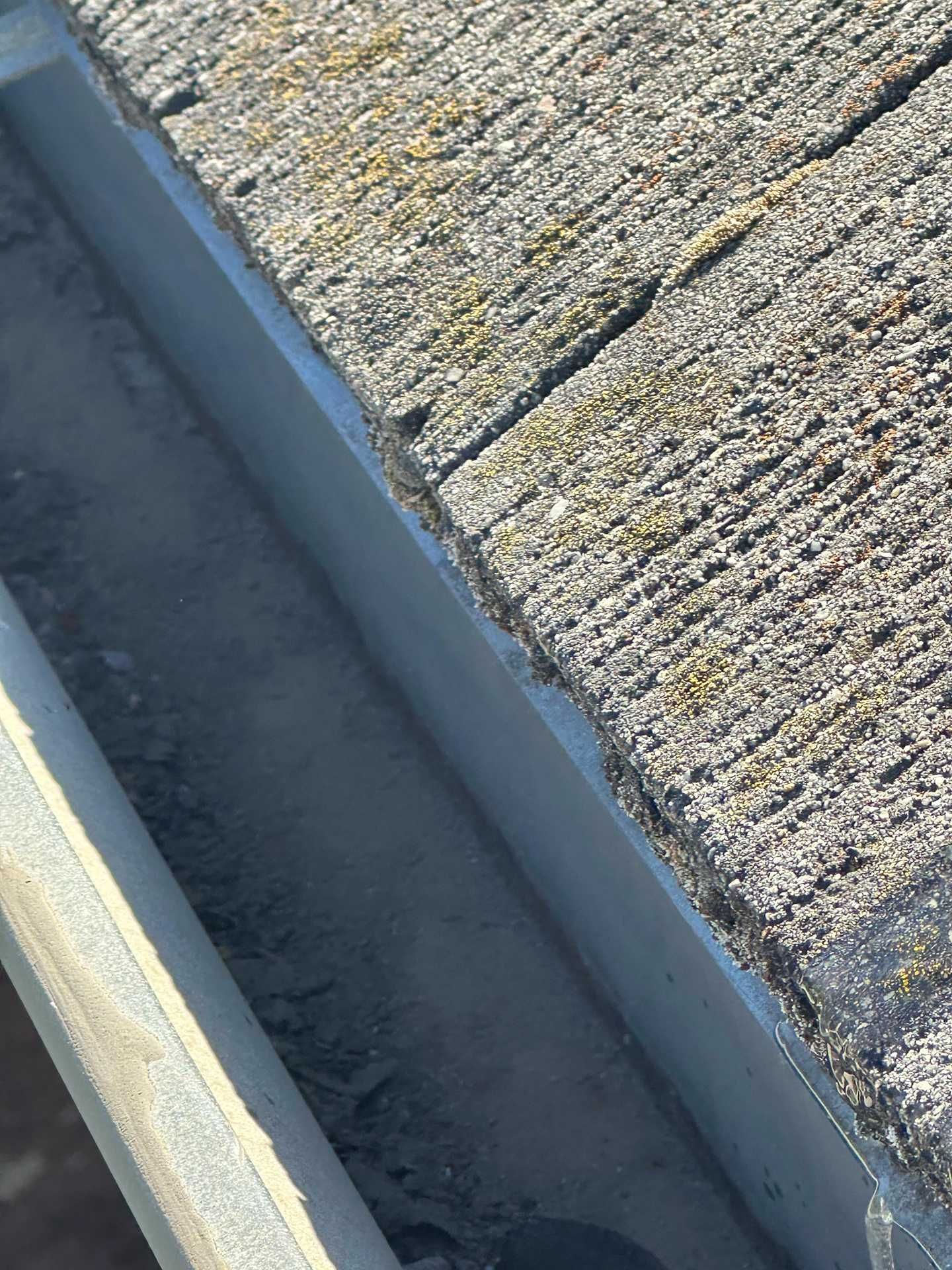 Close-up of a rooftop gutter beside textured concrete tiles with a bit of snow or frost nearby