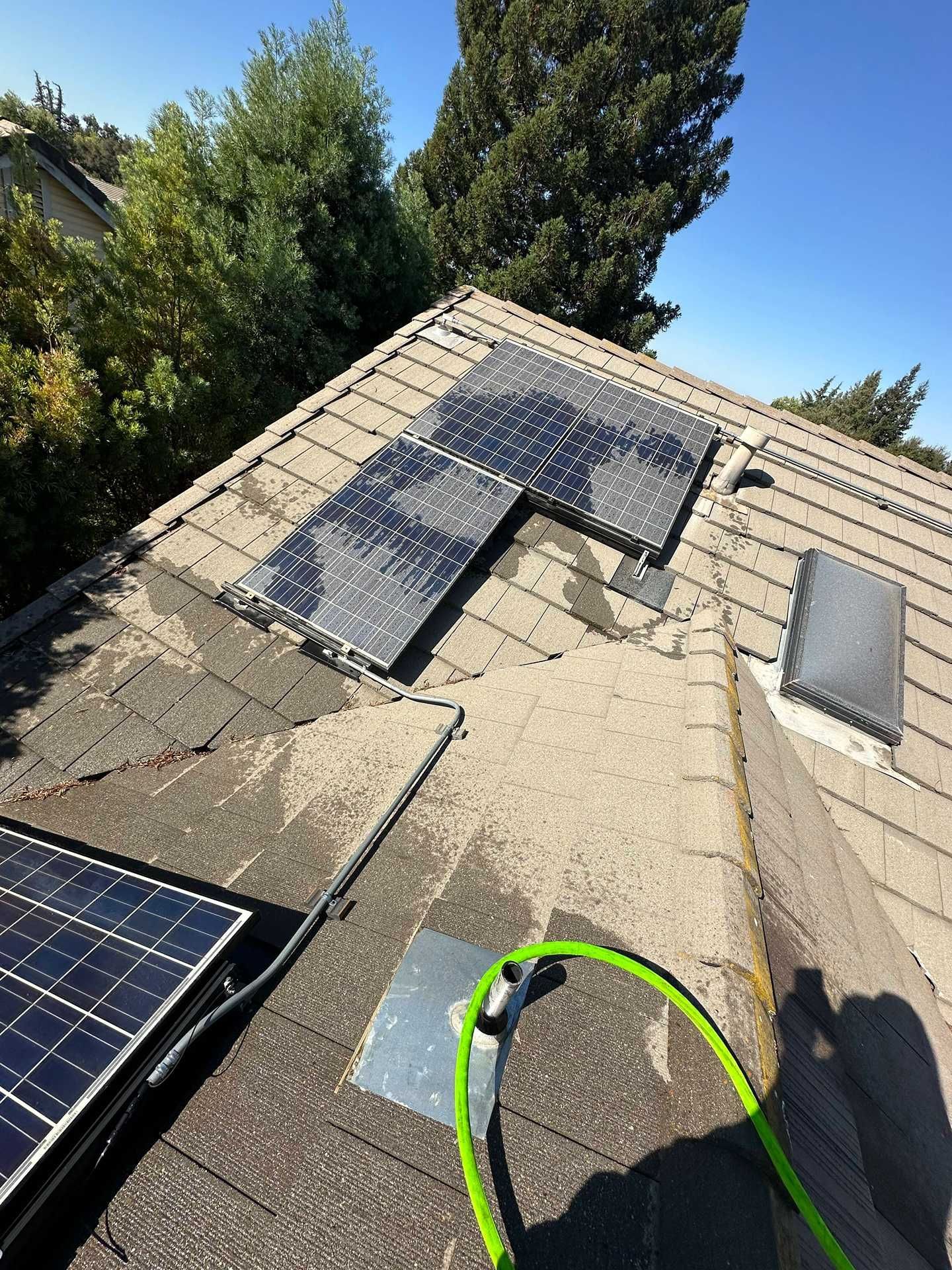 Roof with solar panels under installation, seen at an angle with a green hose in the foreground