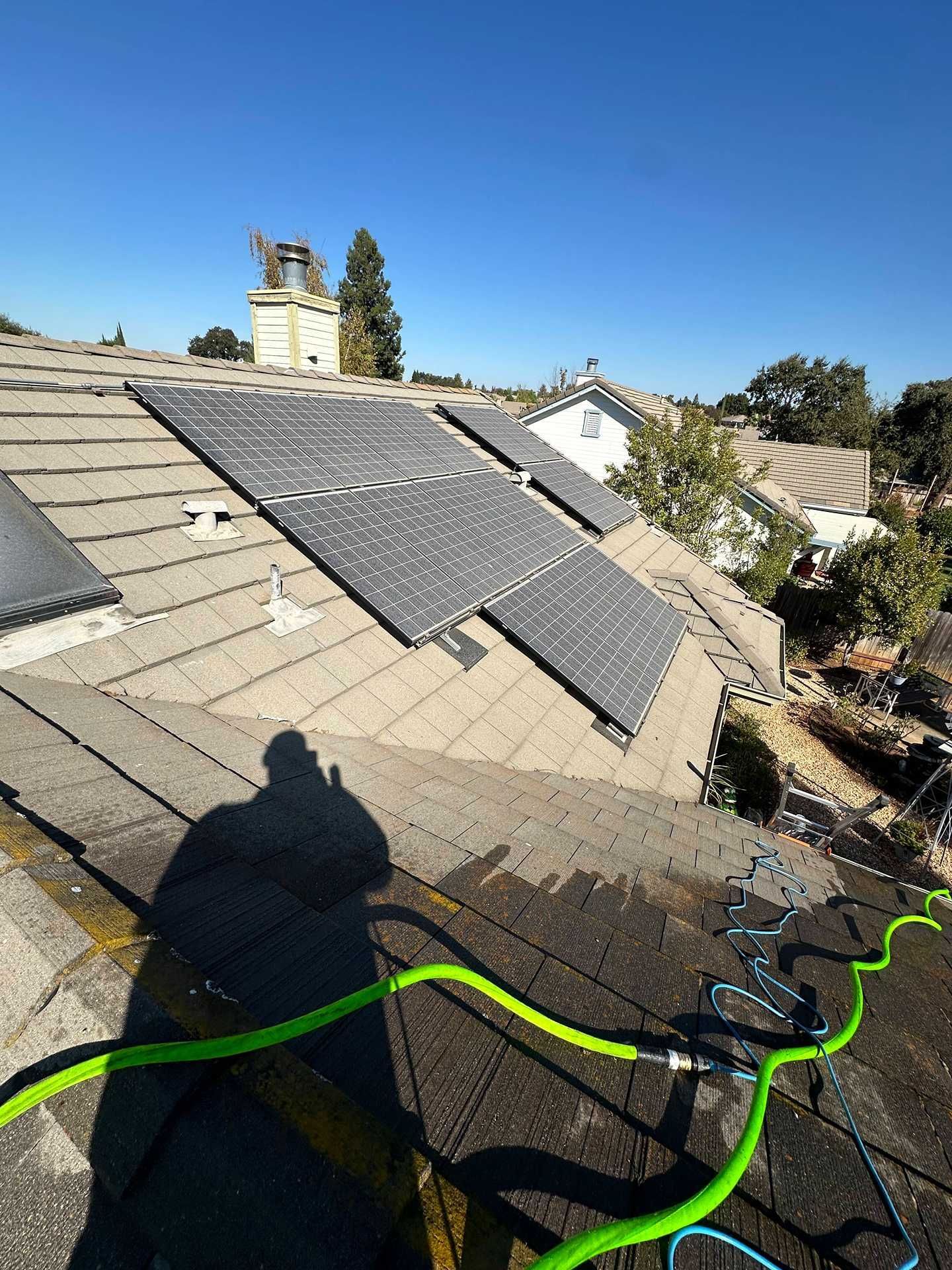 Solar panels on a sloped rooftop with green cable under a clear blue sky.