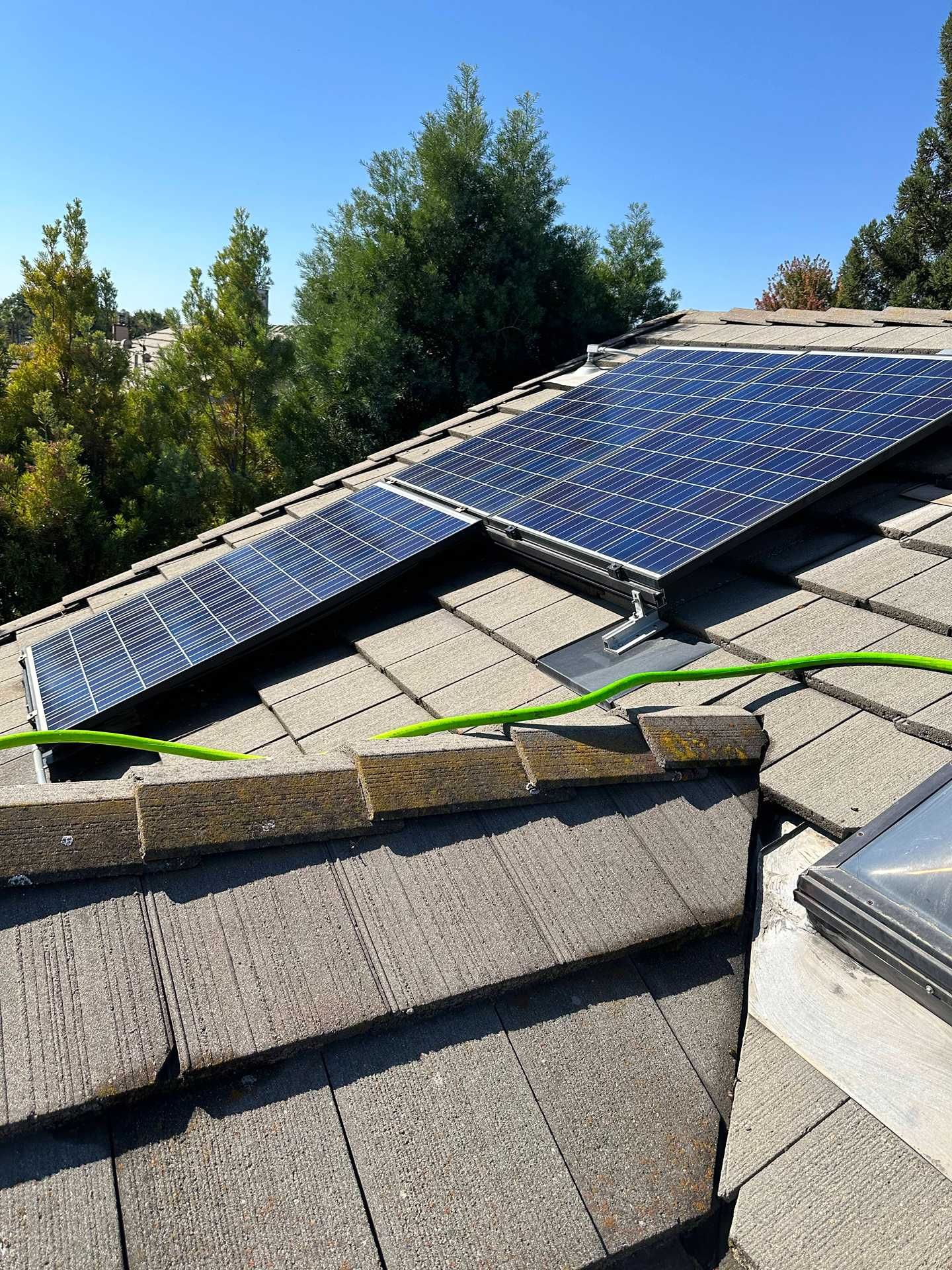 Rooftop solar panels on a sloped gray shingle roof under a clear blue sky.
