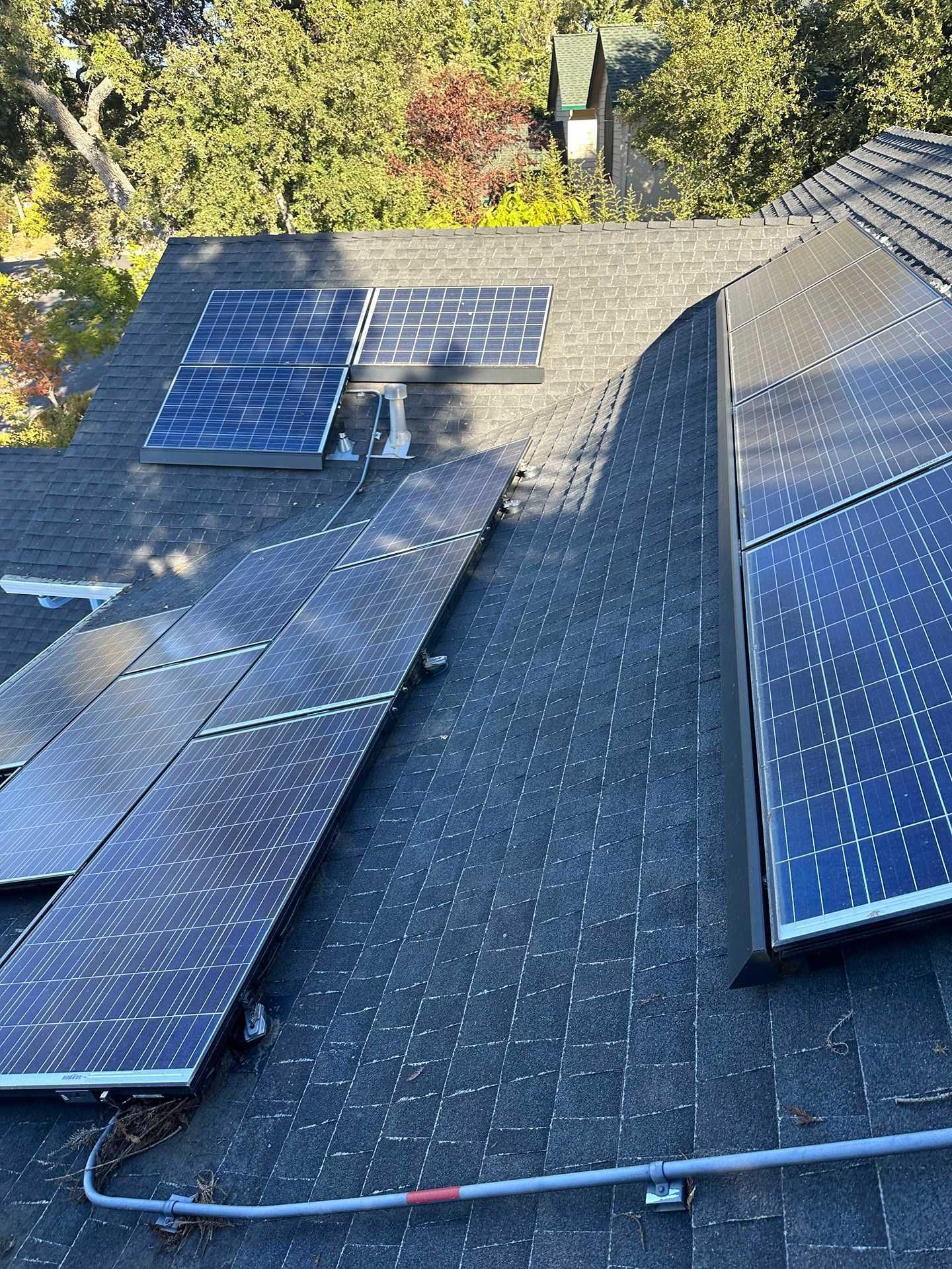Solar panels installed on a dark shingled roof, with trees visible in the background.