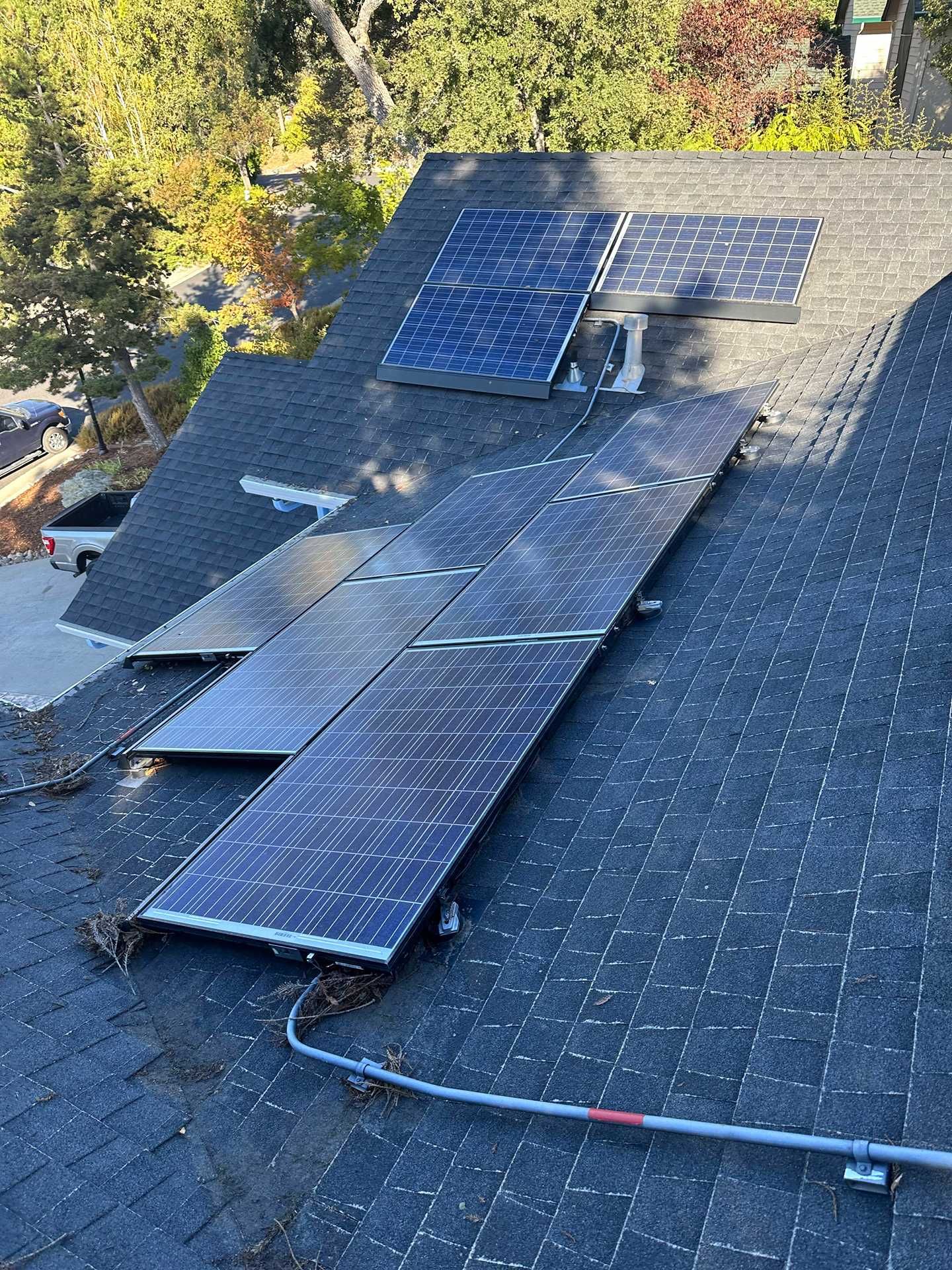 Roof with several blue solar panels and a visible cable on gray shingles, viewed from above