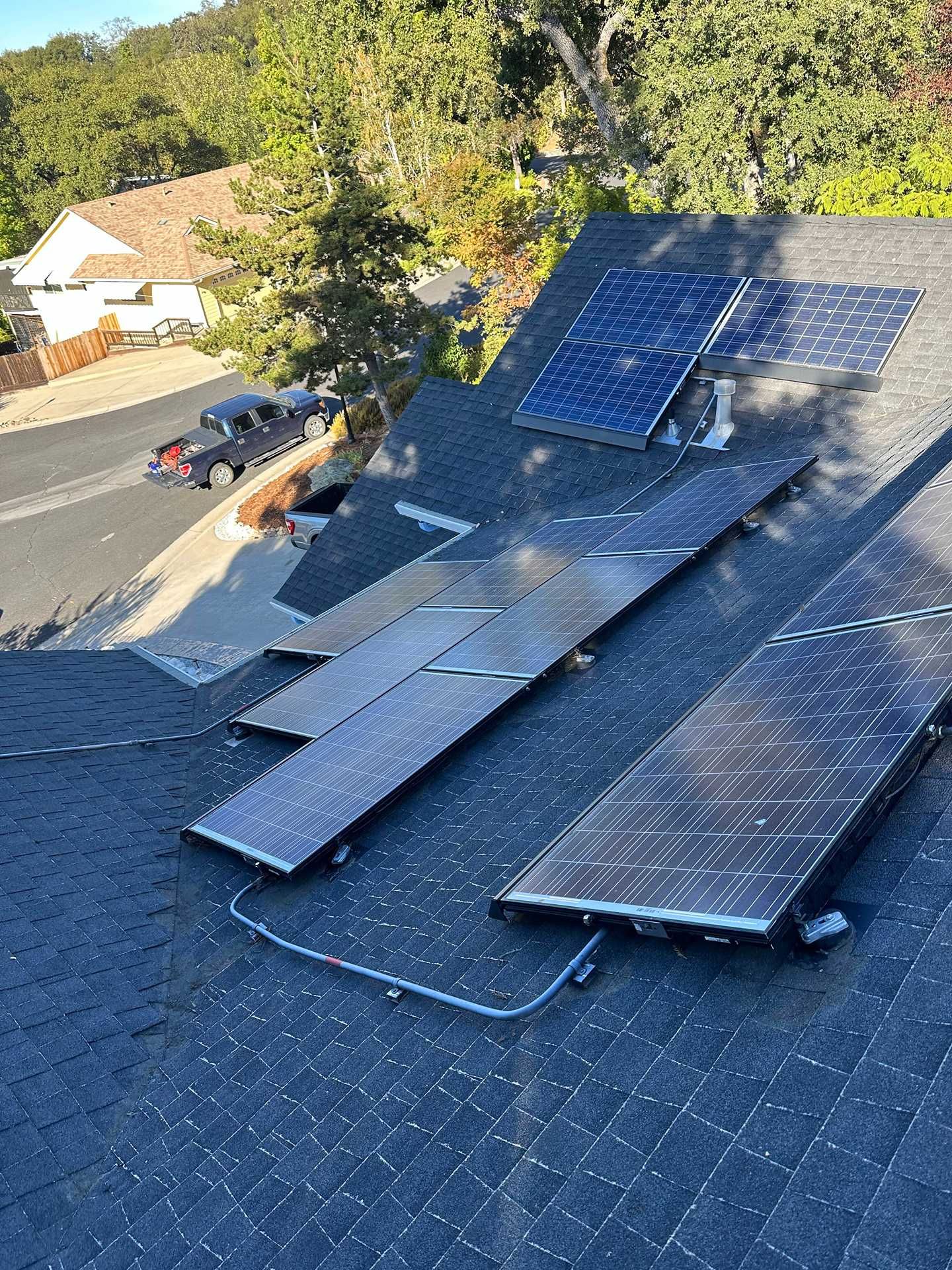 Damaged solar panels scattered across a shingled roof with one panel propped upright after a storm