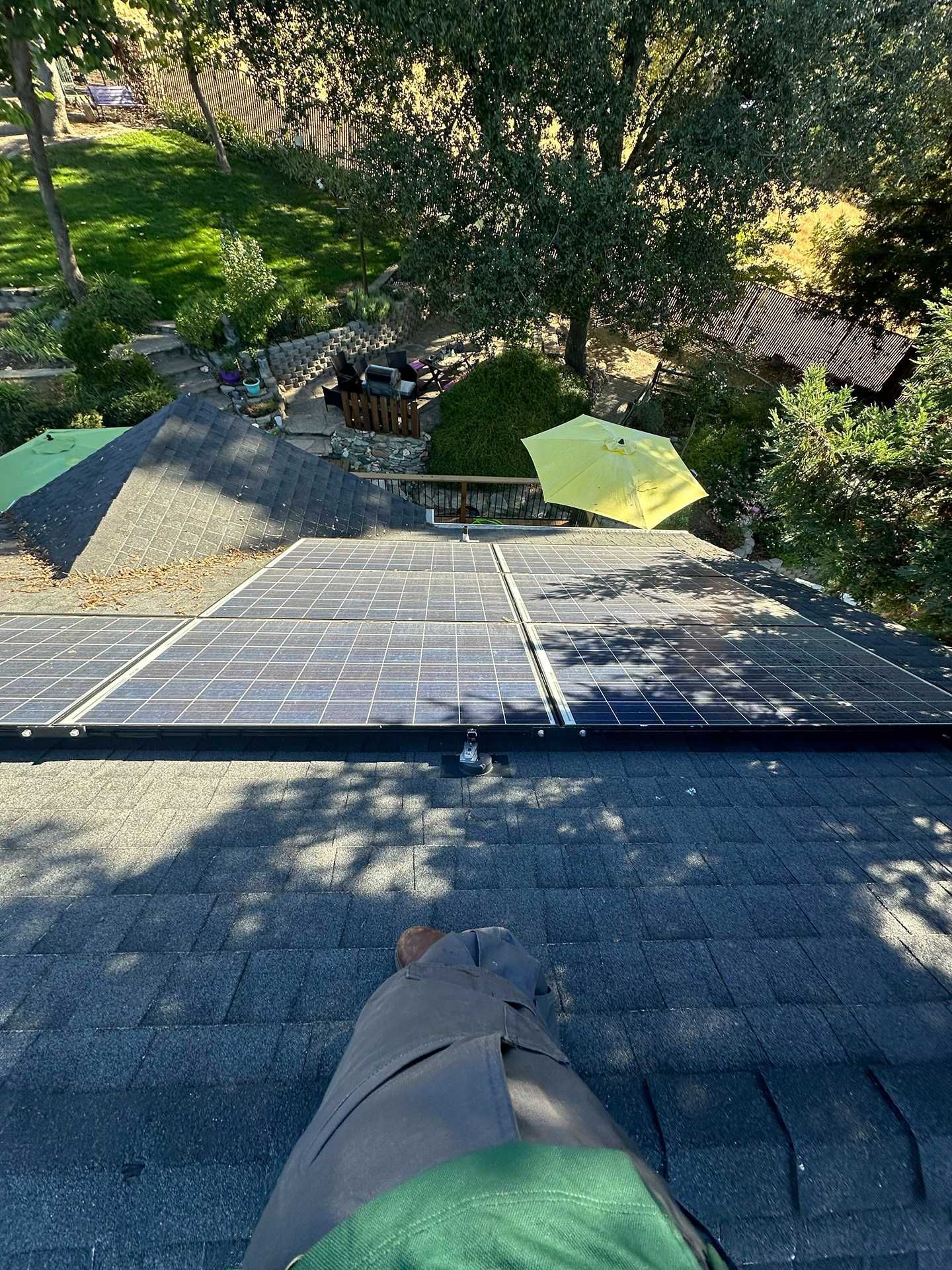 Rooftop view with solar panels overlooking a sunny backyard with patio tables and chairs.