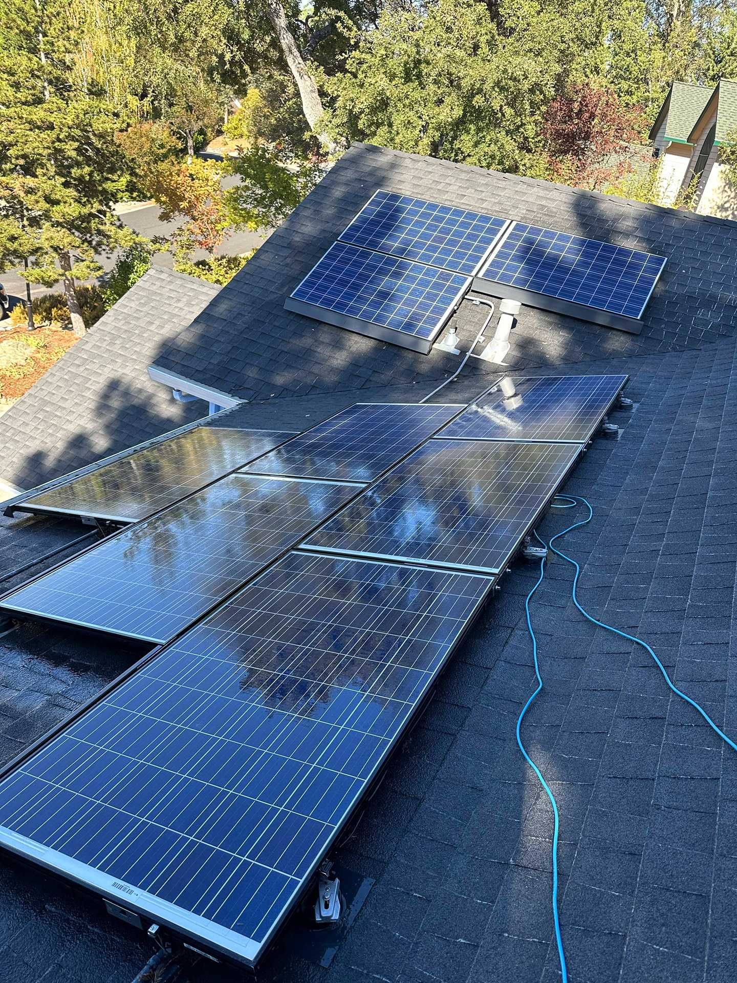 Solar panels spread across a roof, with wires and trees in the background.