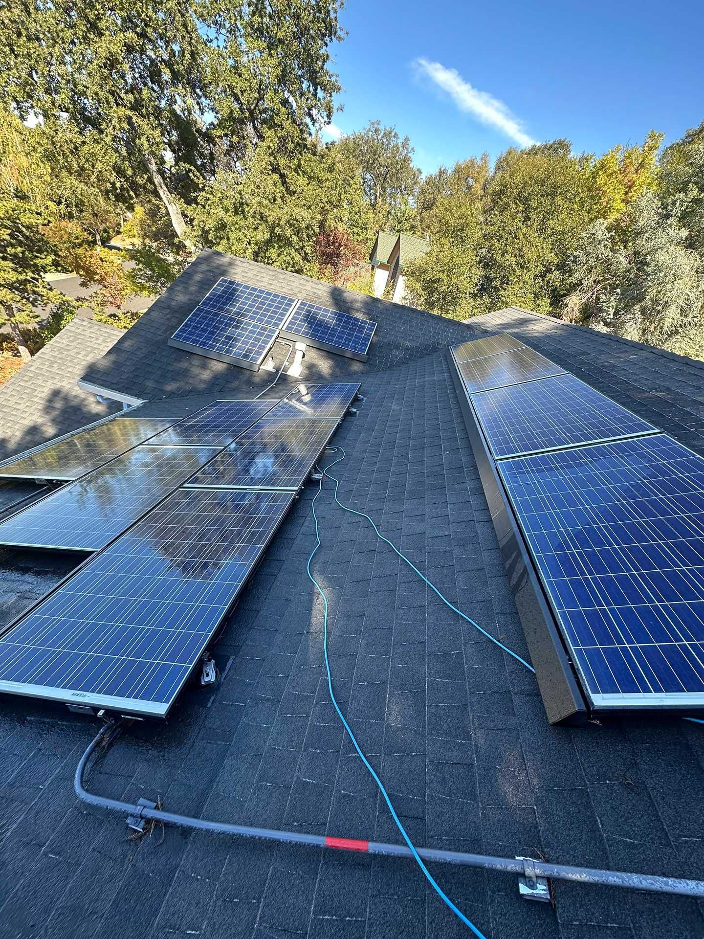 Solar panels installed on a sloped roof in a wooded area, with a person working near the ridge.