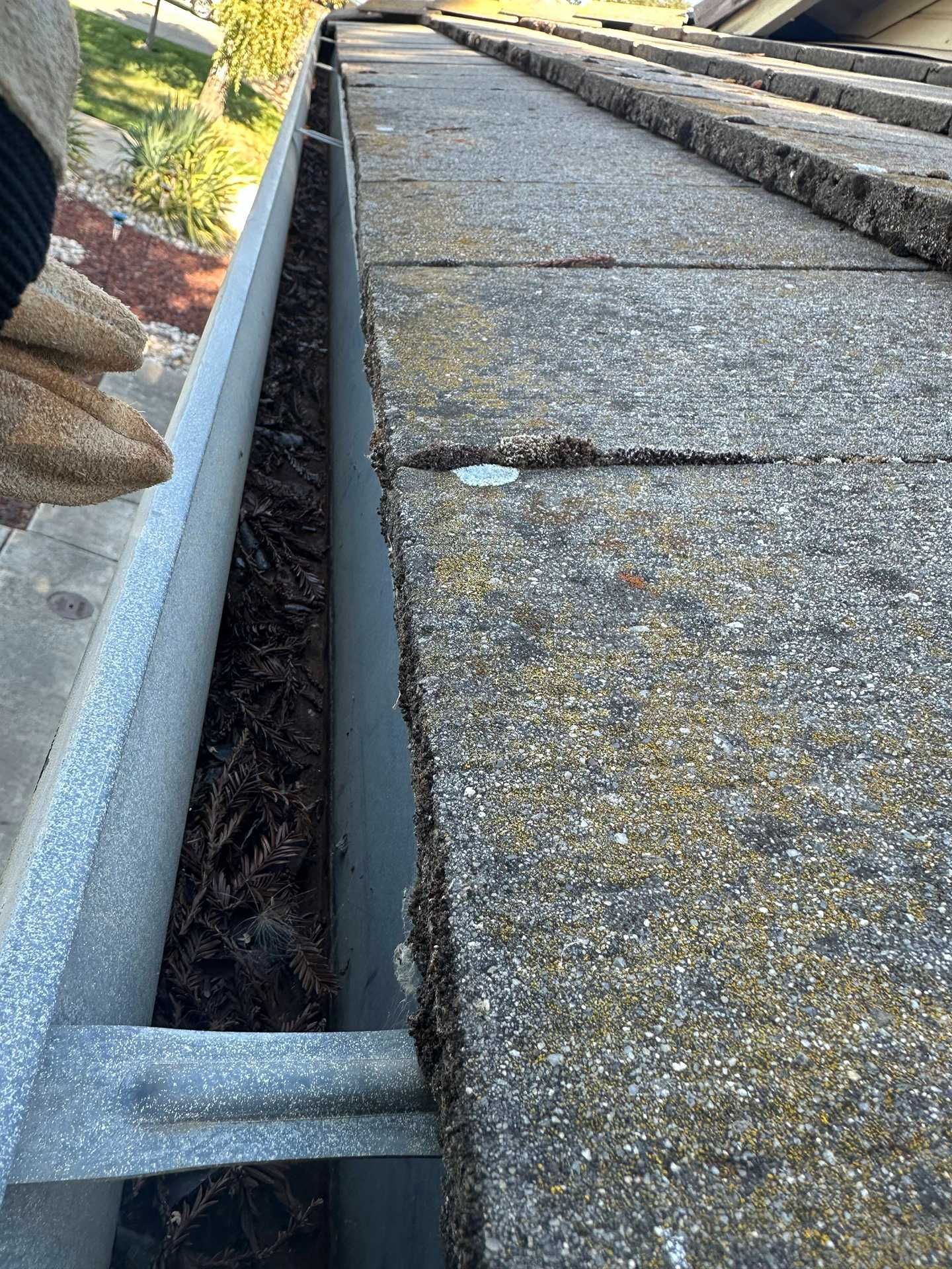 Close-up of a roof gutter and downspout beside a gravel roof edge and stone walkway.