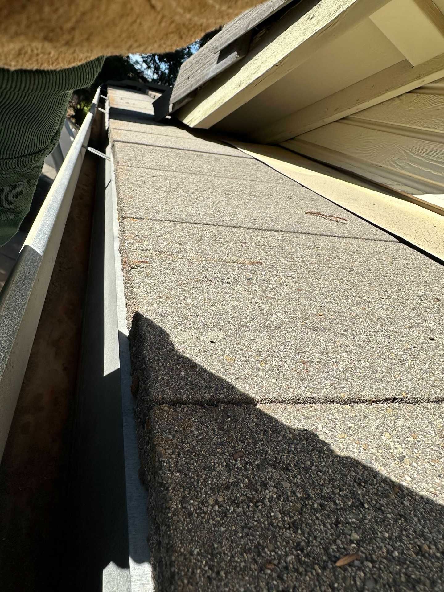Steep shingled roof beside a house wall, viewed from above with strong sunlight and shadows