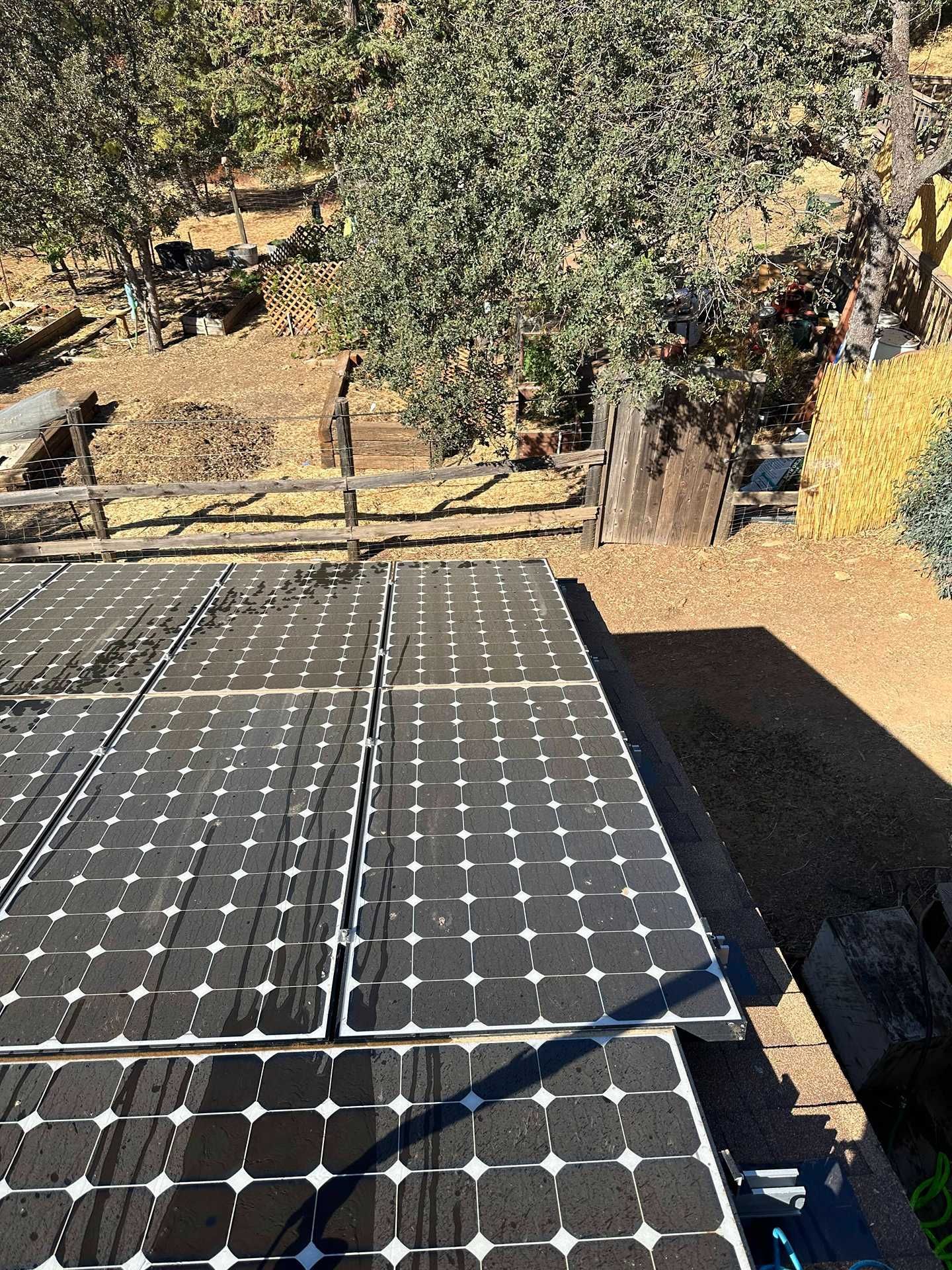 Solar panels on a rooftop with trees and a yard in the background.