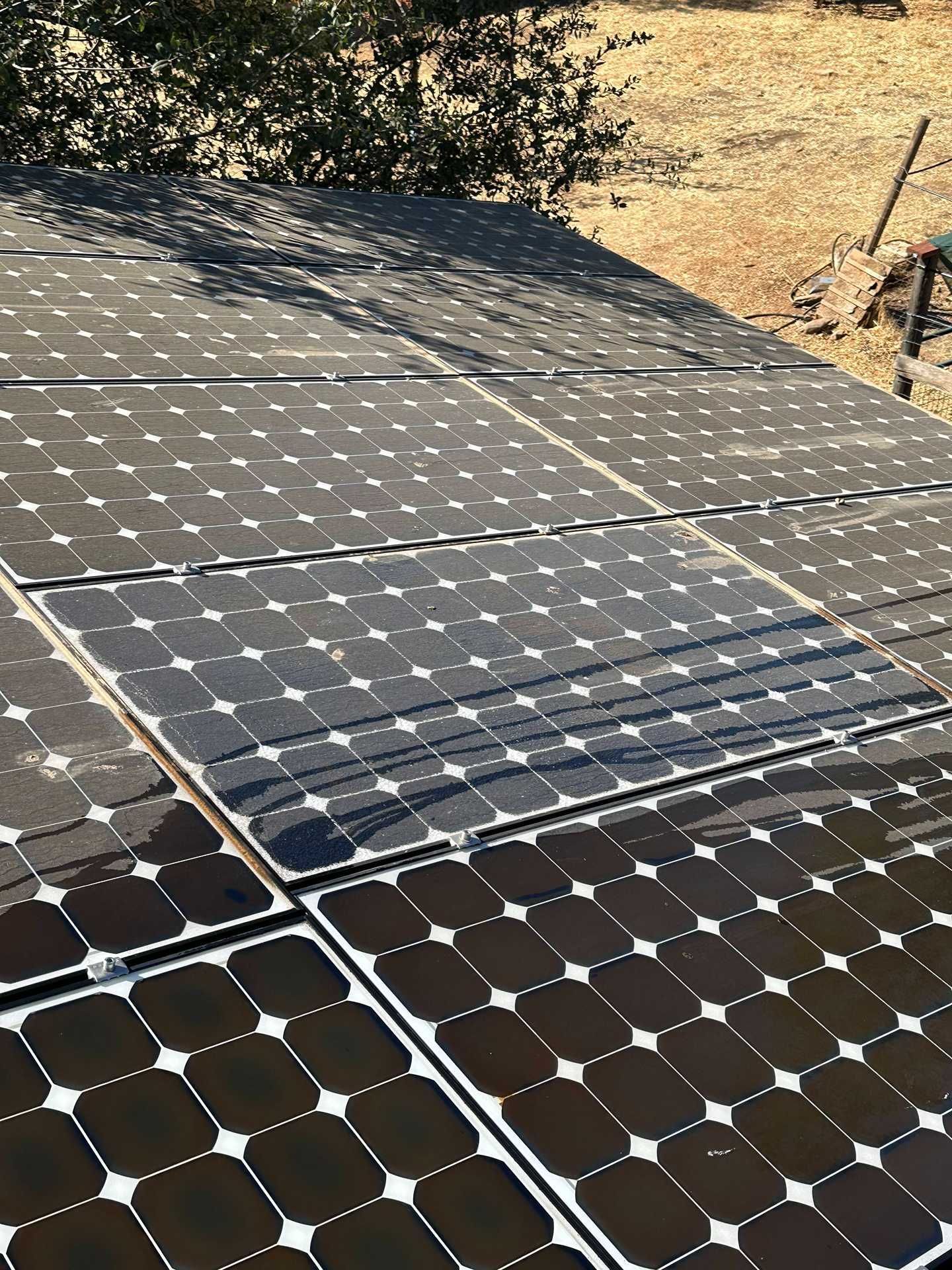 Solar panels installed on a sloped rooftop beside a dirt hillside in bright sunlight
