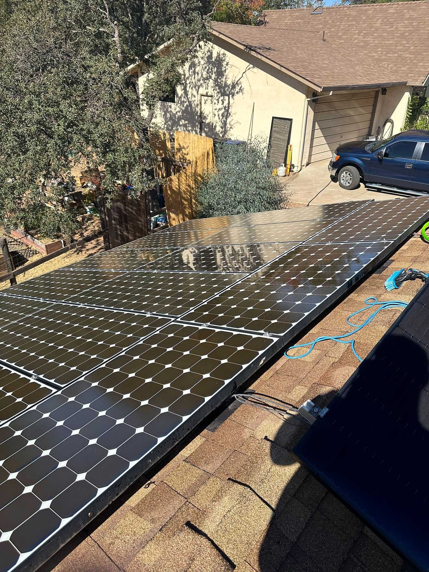 Solar panels laid across a roof beside a beige house and a blue car in a sunny yard