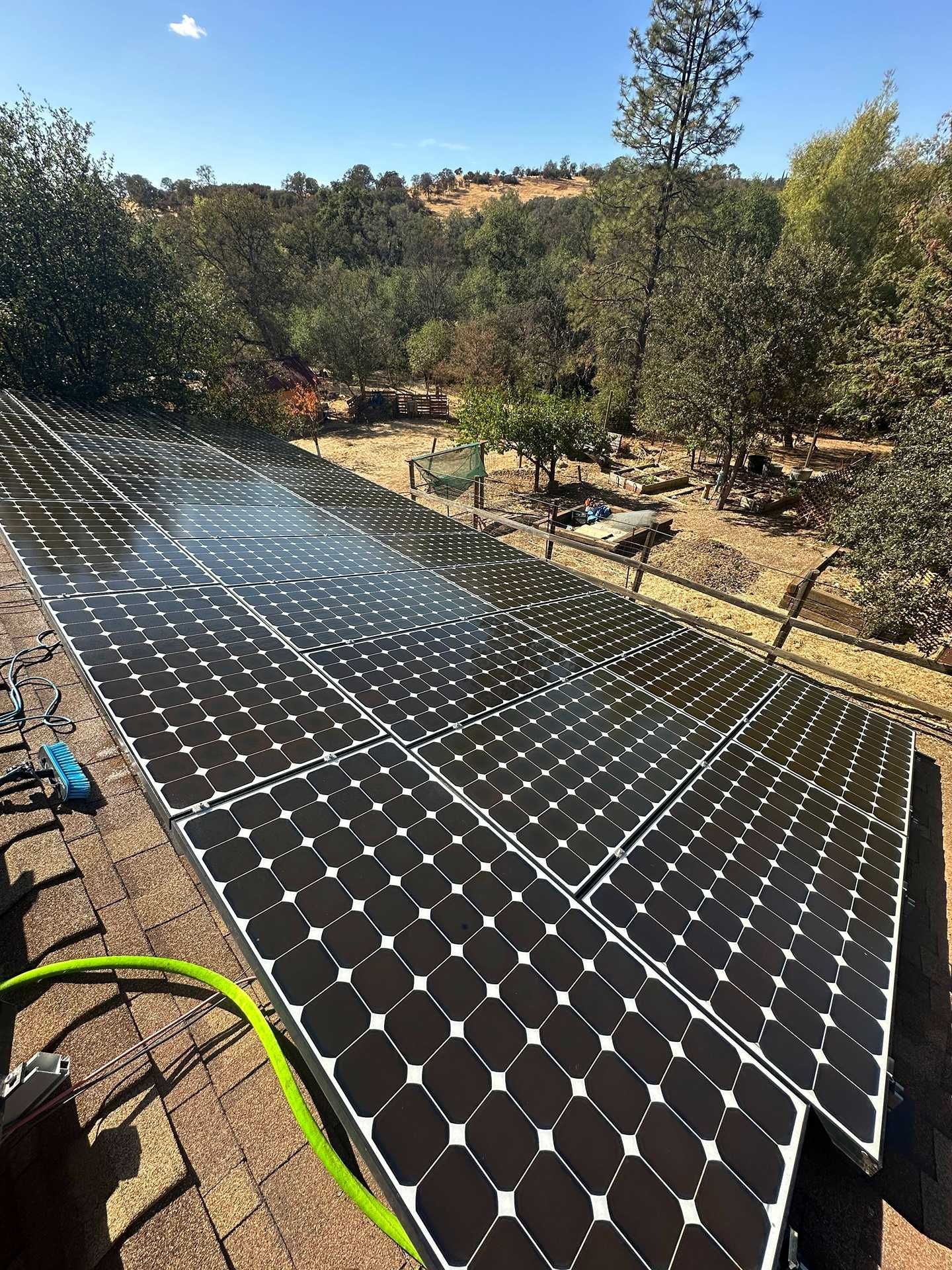 Solar panels installed on a sloped roof in a sunny, wooded outdoor setting.